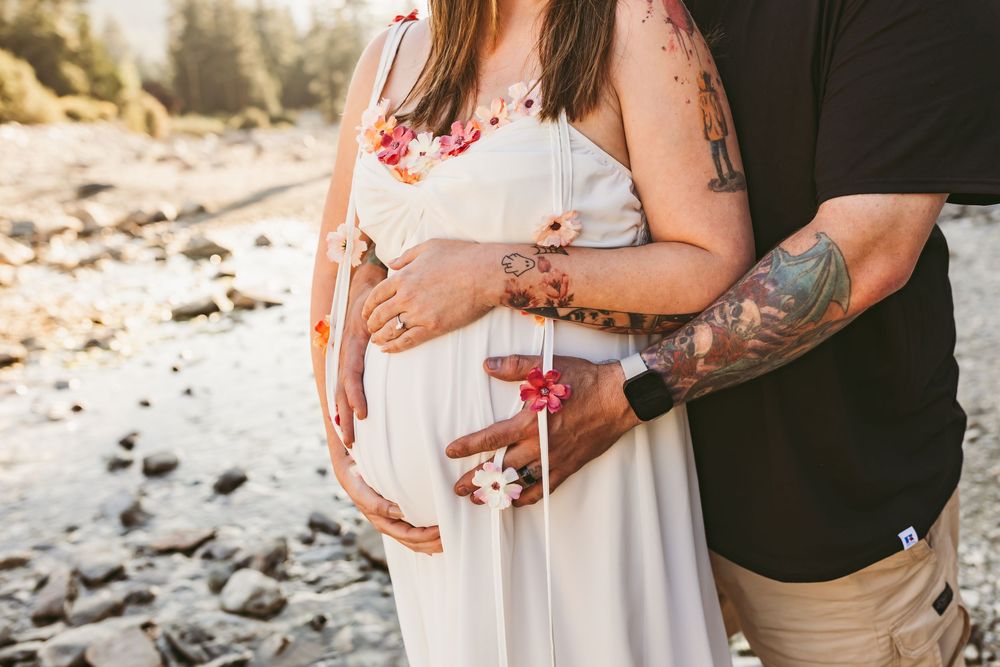 Maternity photoshoot scene showing couple embracing on rocky beach in romantic casual attire.