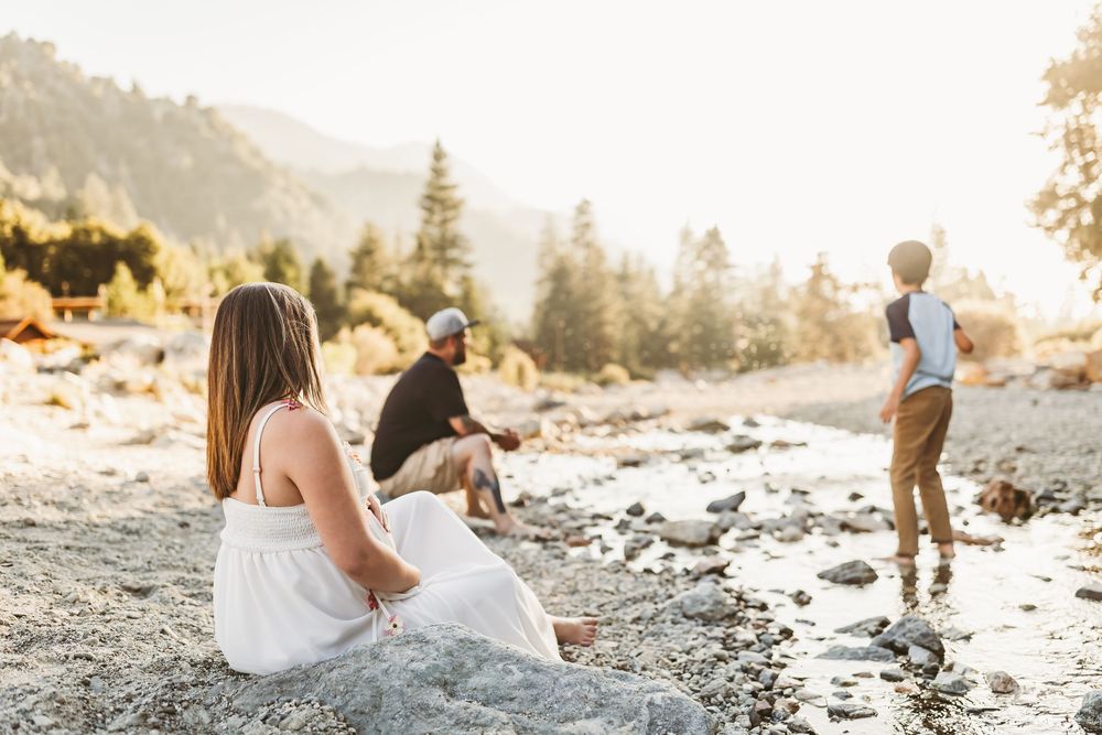 A couple sits together on a rocky beach in golden sunlight during a romantic sunset photo session.