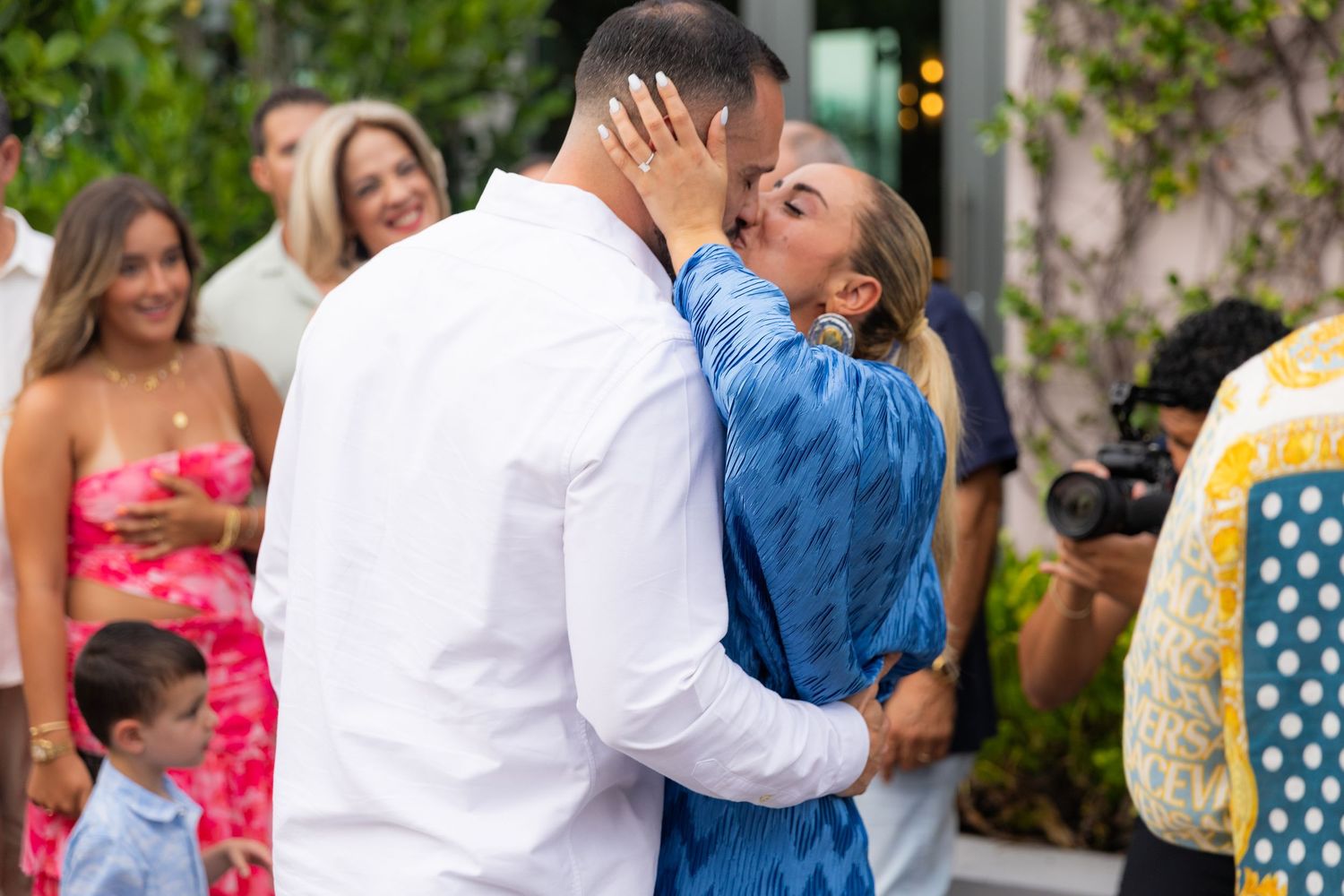 A celebratory moment captured during an outdoor proposal with guests watching.