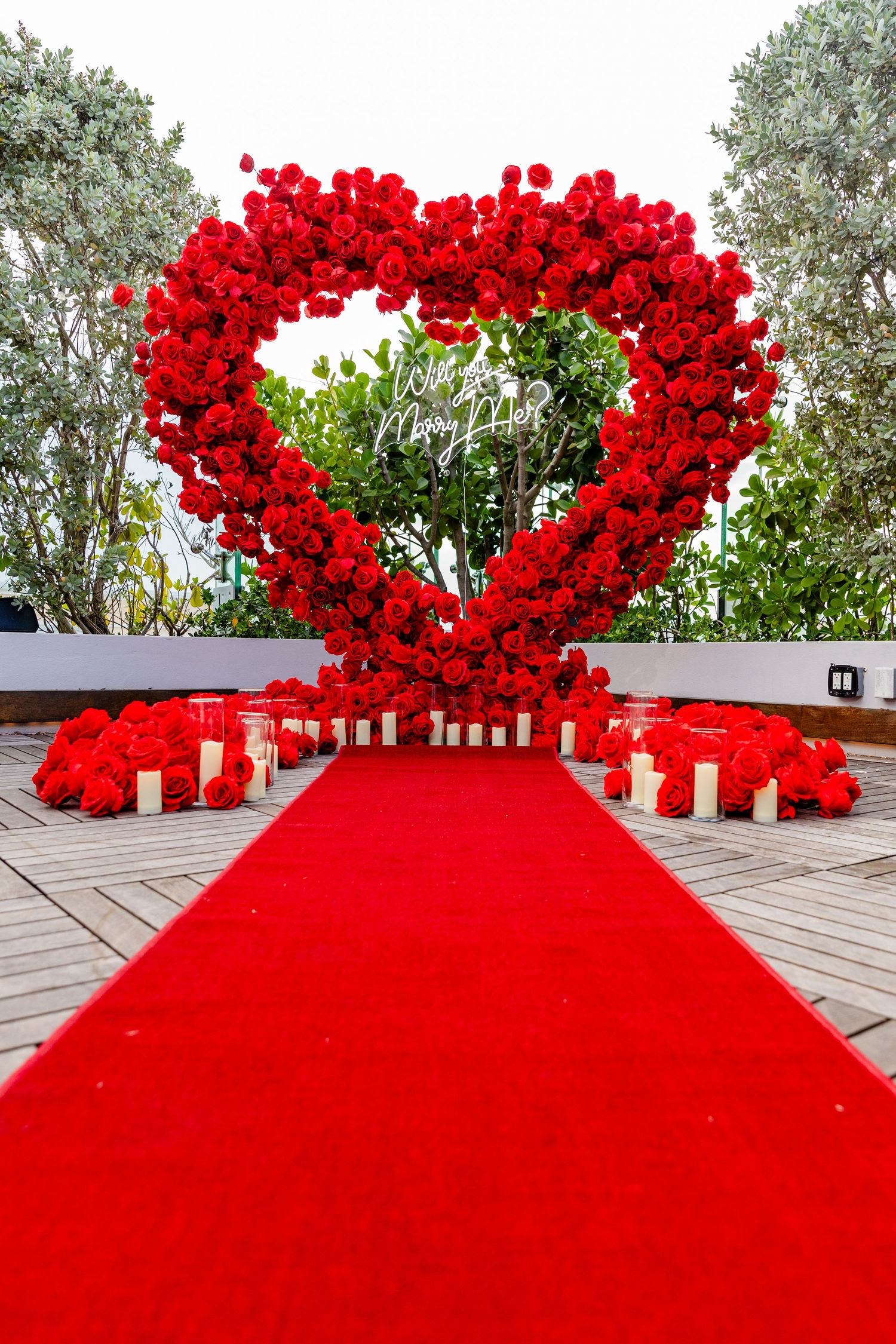 A decorative heart-shaped arch made of vibrant red roses with a red carpet path leading through it.