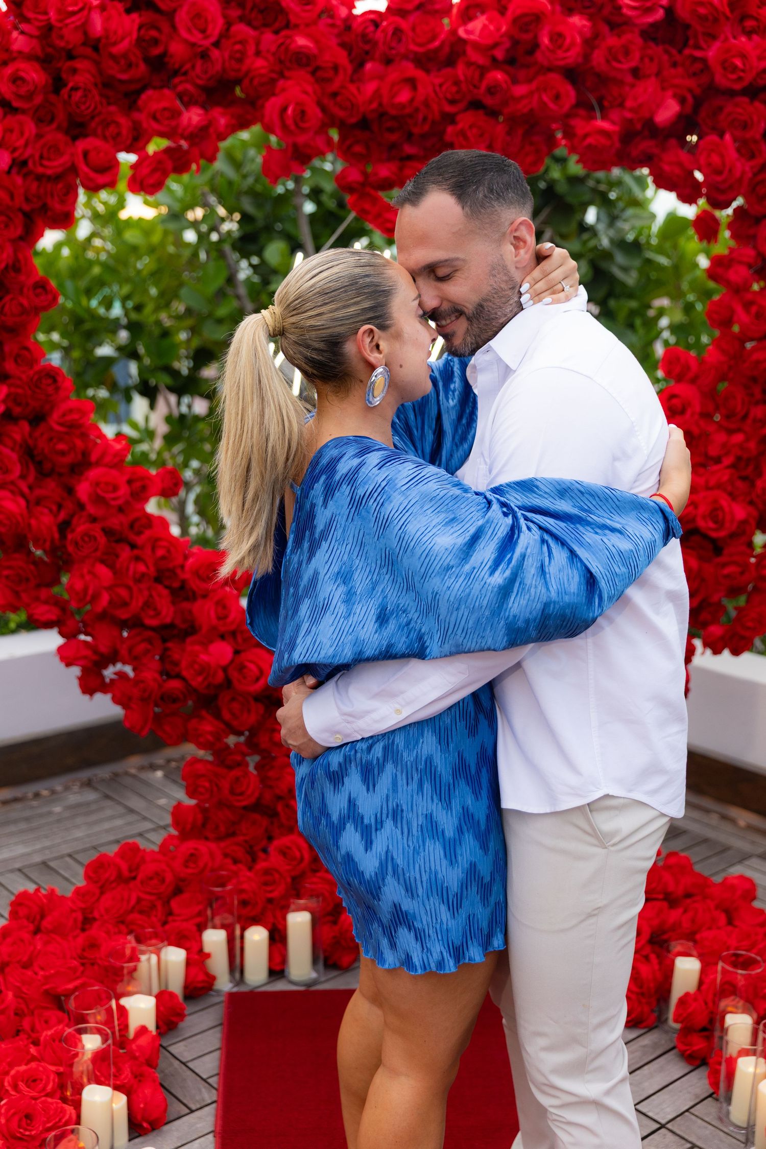 Romantic scene with a couple sharing a moment beneath a wall of red roses and candlelight.