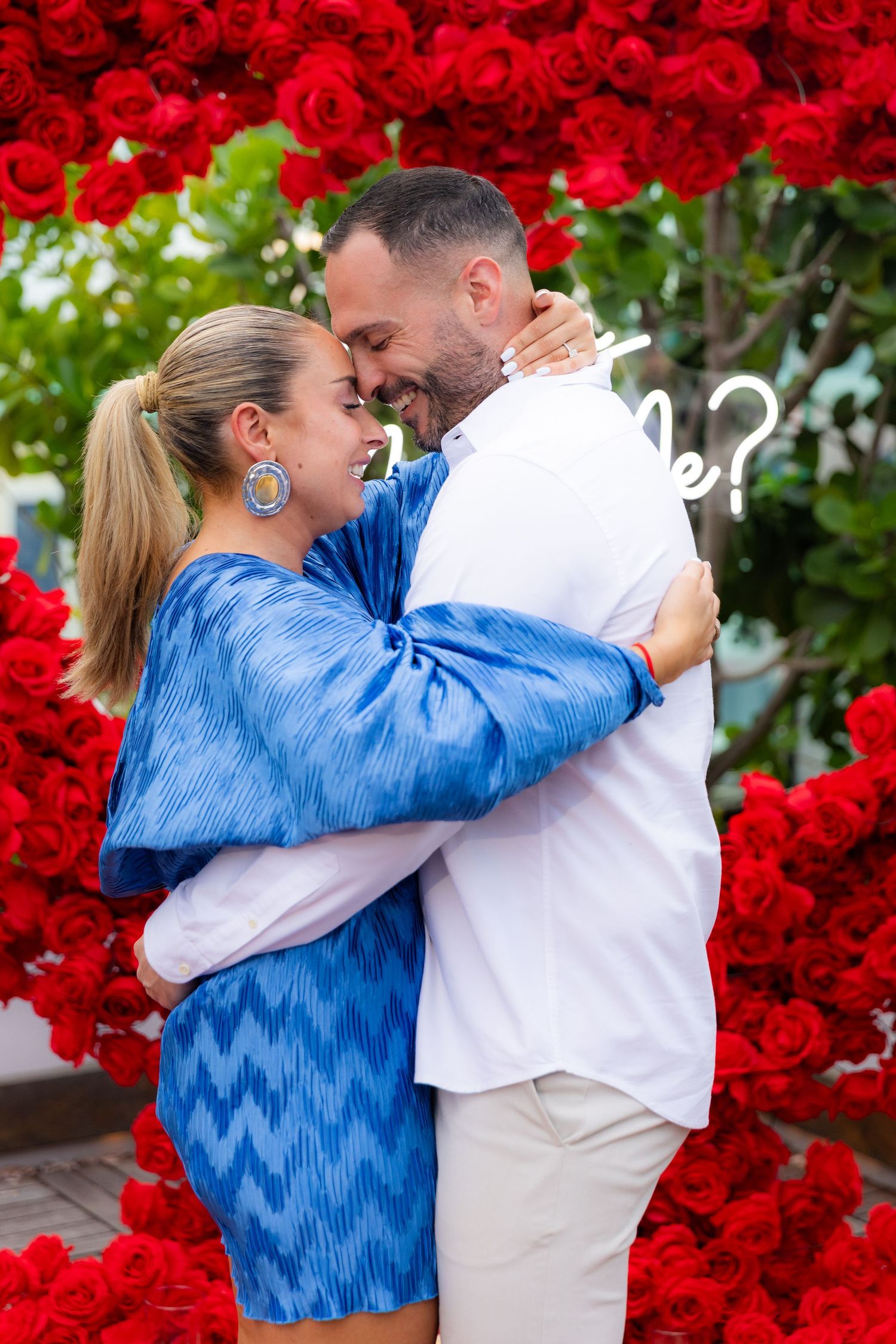 A joyful embrace captured in front of a stunning red rose heart display.