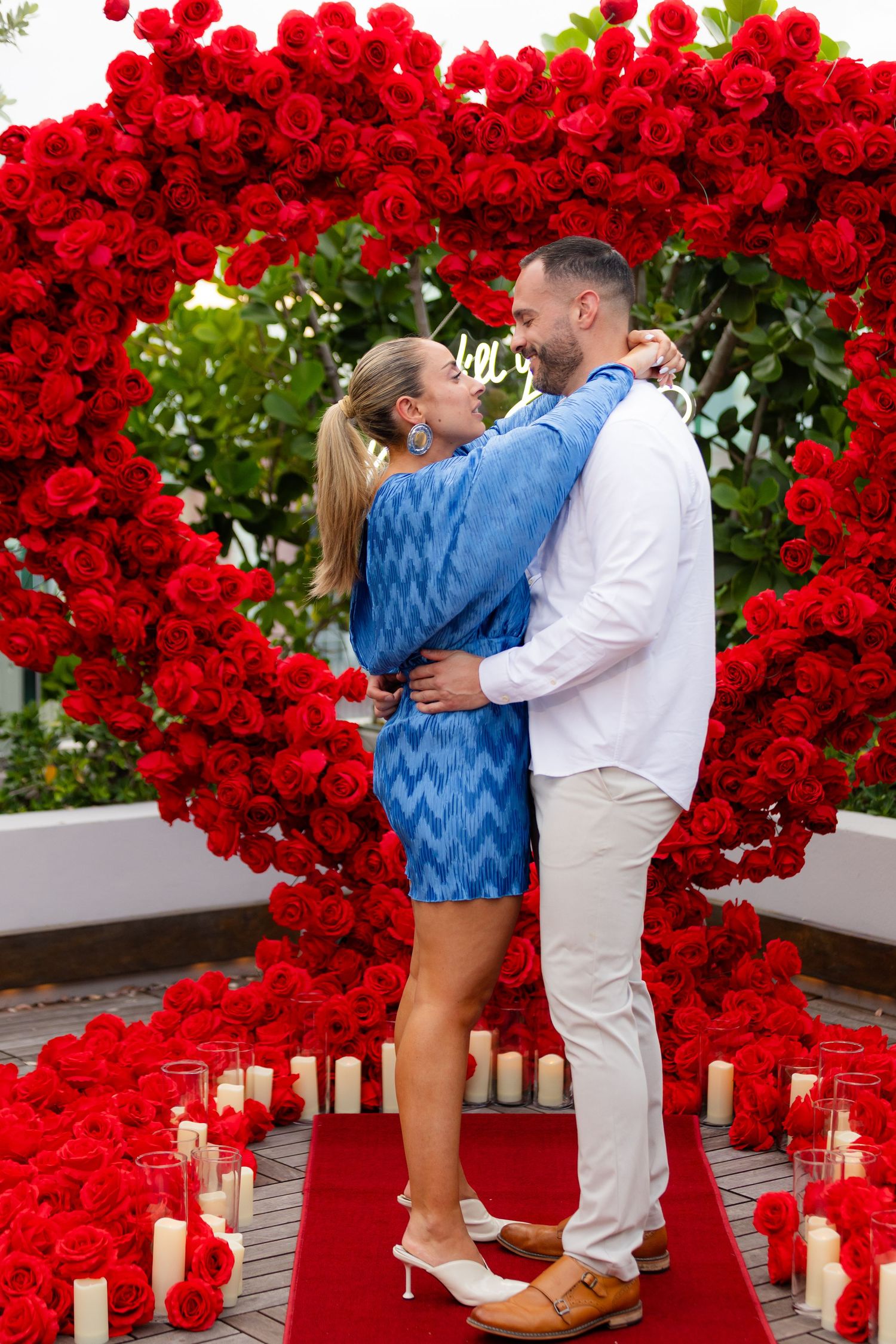 A heart-shaped arch made of vibrant red roses creates a romantic backdrop on an outdoor terrace.