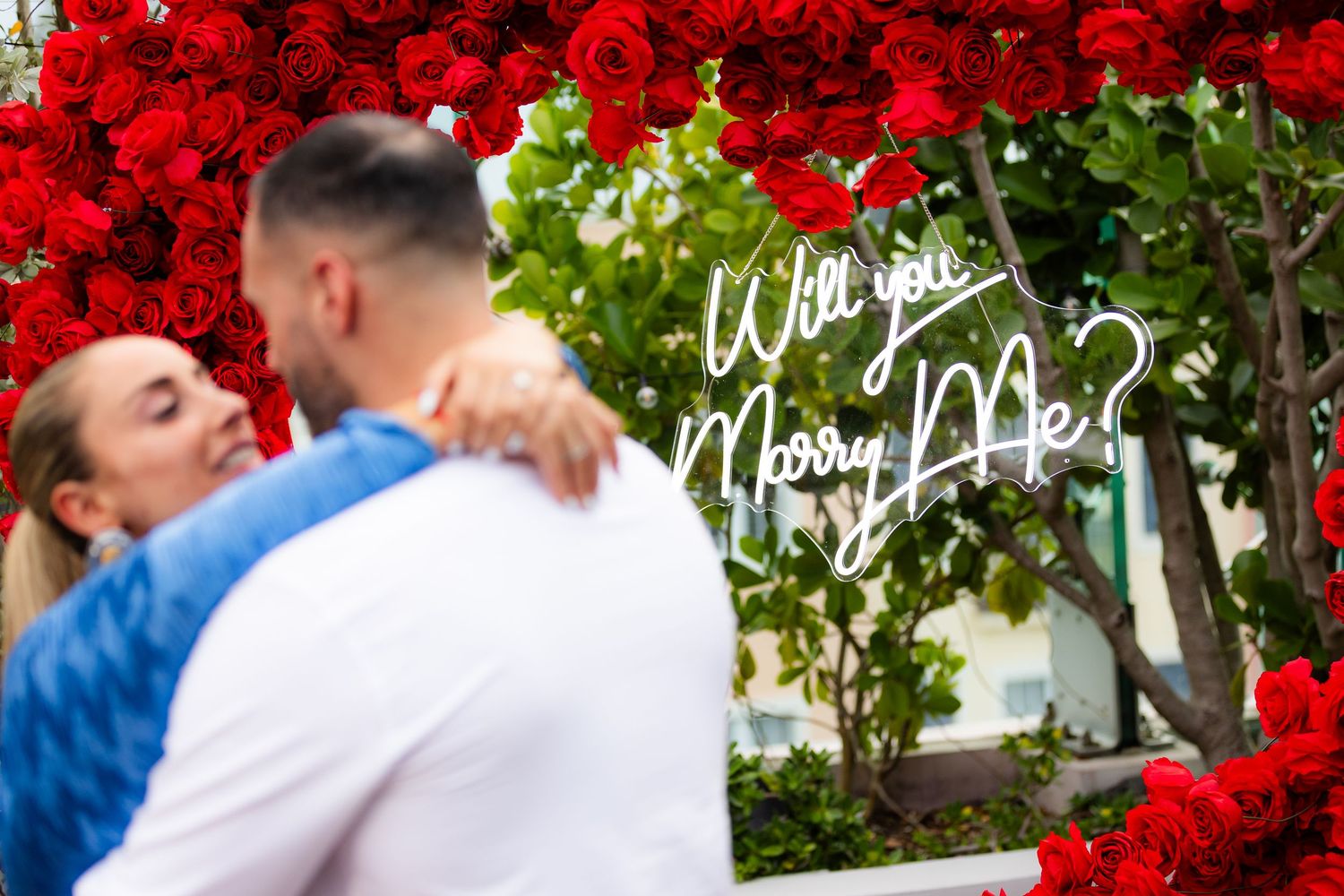 A romantic moment captured under a stunning arch of red roses with glowing candles.