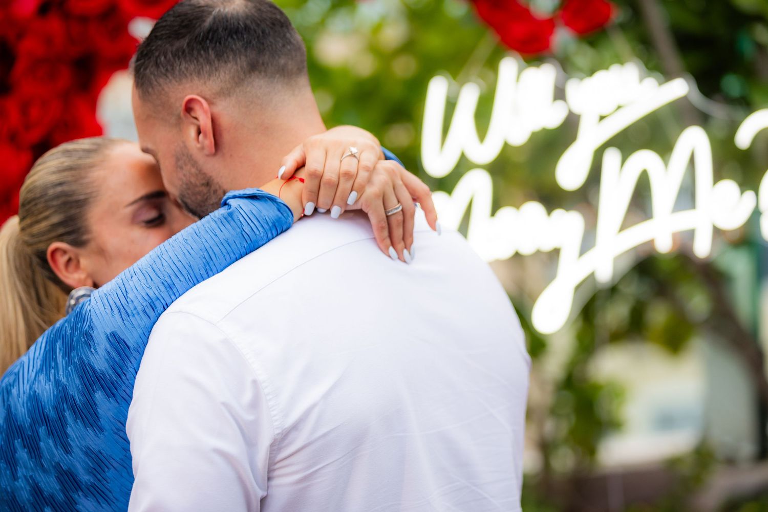 A couple embraces beneath an elaborate display of red roses during a special moment.