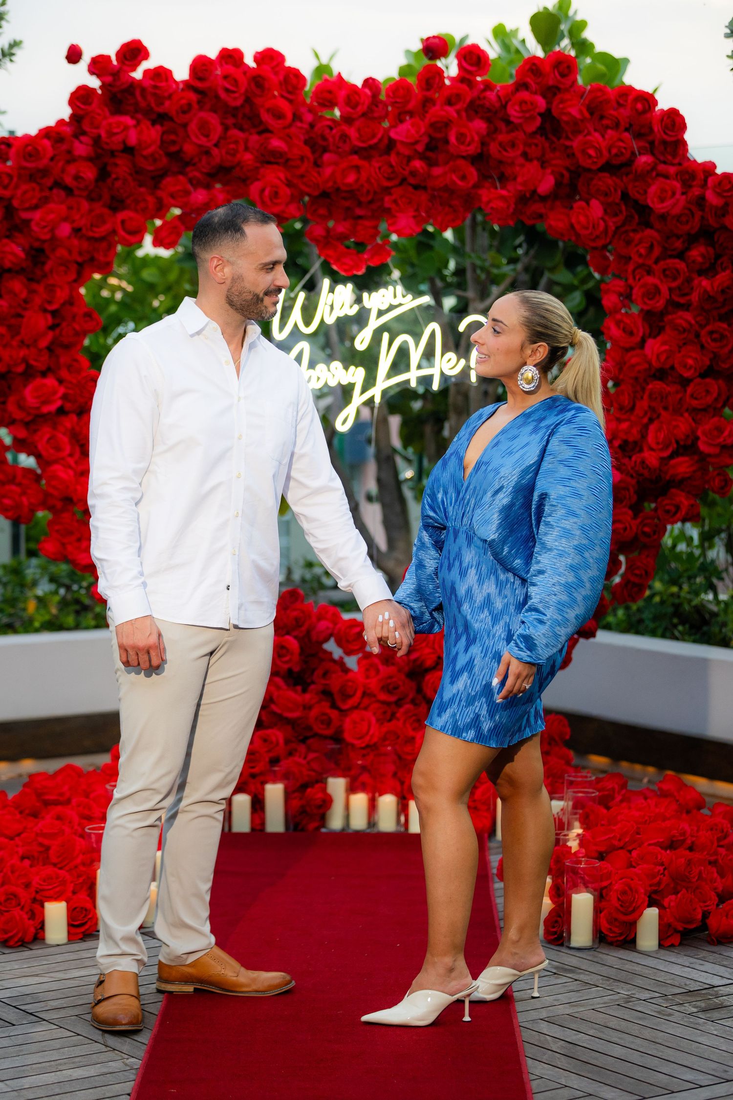 A beautifully decorated proposal setting with red roses, candles, and a wooden deck.