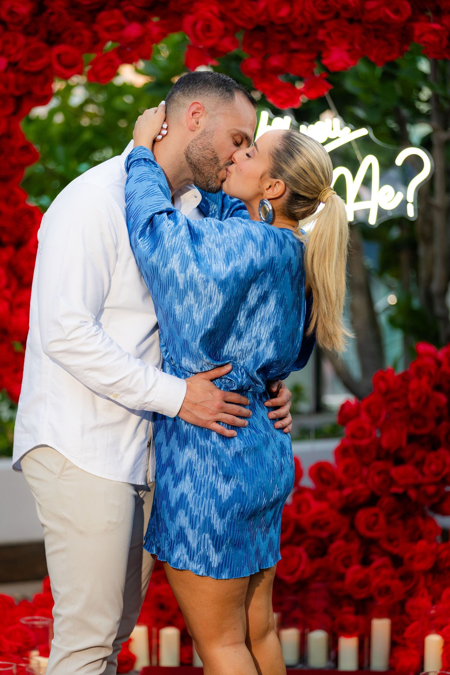 A couple shares an intimate moment surrounded by a beautiful red rose heart-shaped installation.