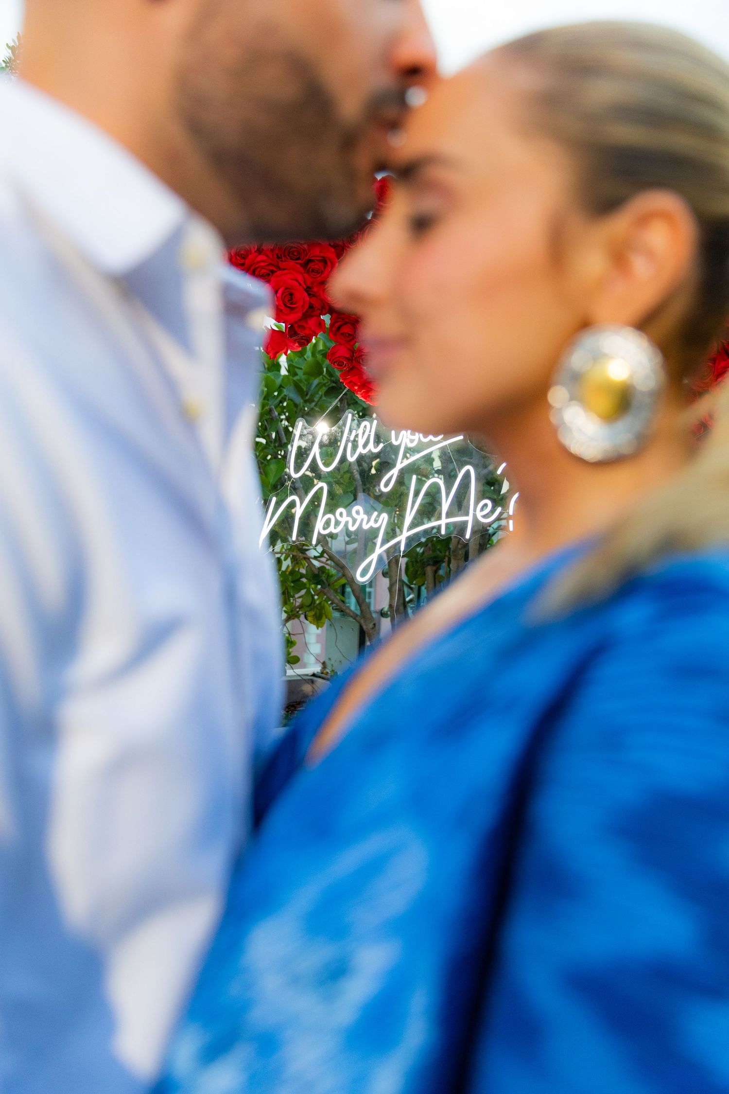 An intimate moment captured against a backdrop of red roses and romantic lighting.