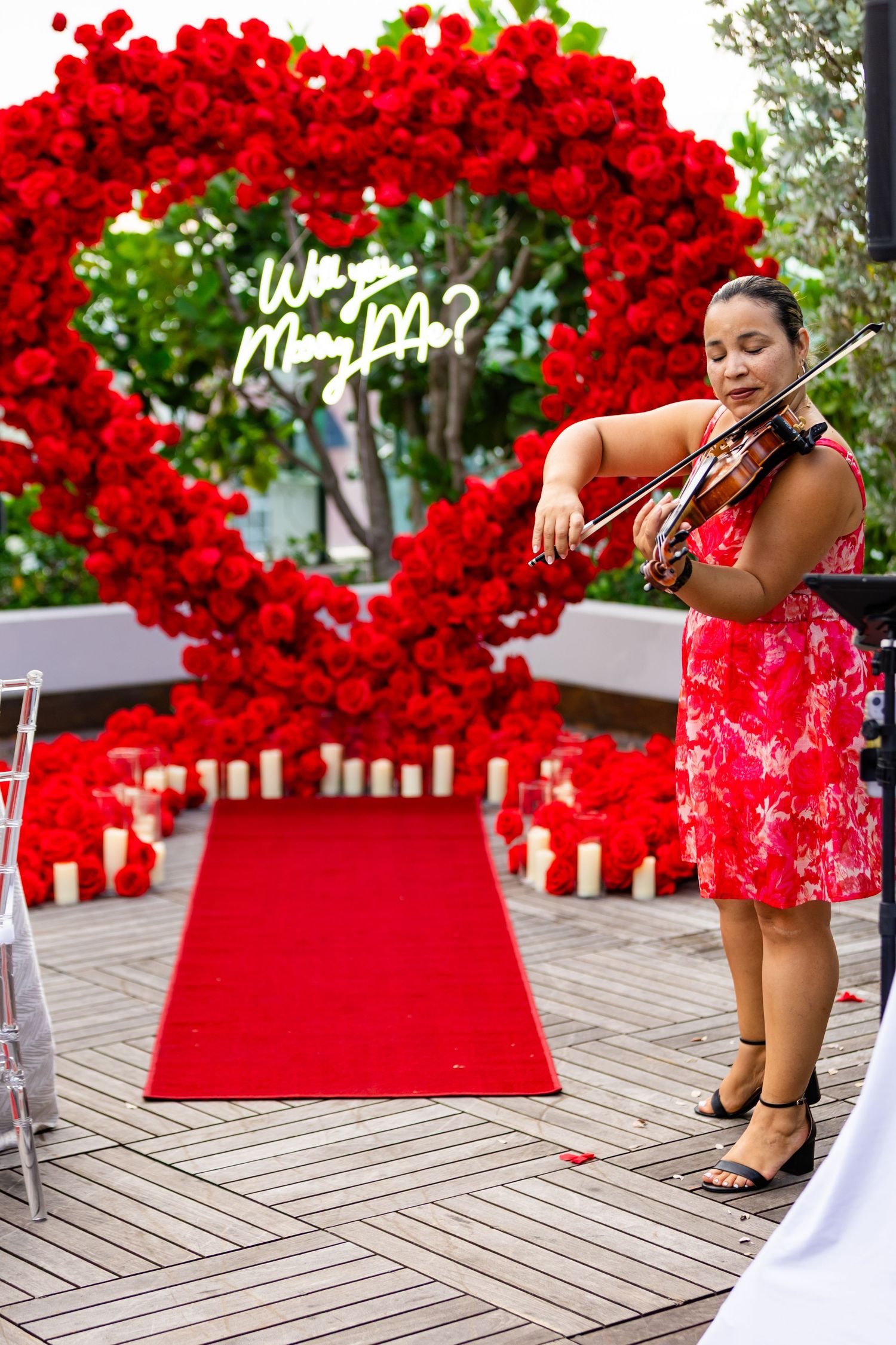 A vibrant red heart-shaped balloon arch installation with white lettering creates a romantic backdrop on a wooden deck.