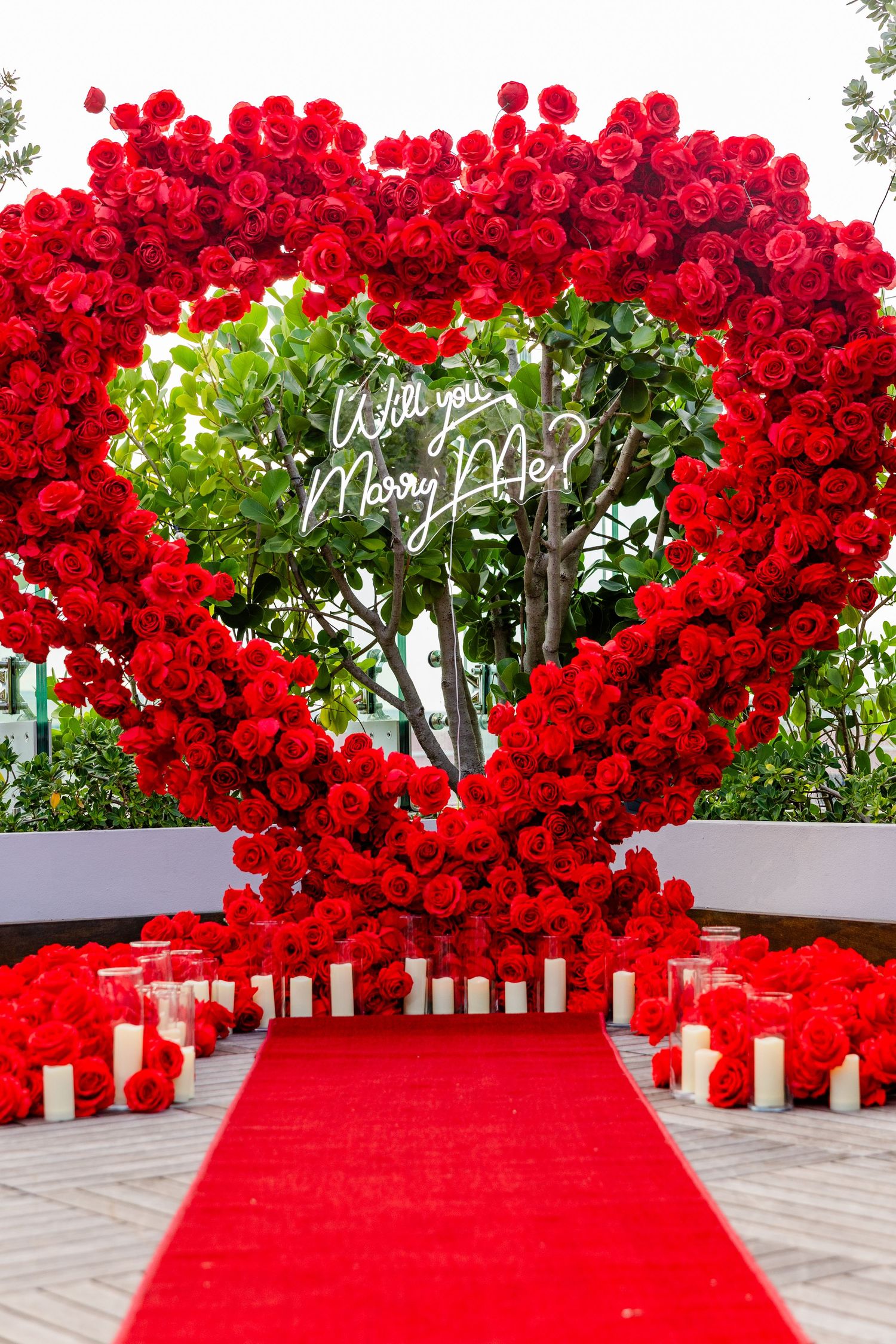 Stunning red rose arch installation with a bright red carpet walkway and glowing candle lanterns creating a romantic path.