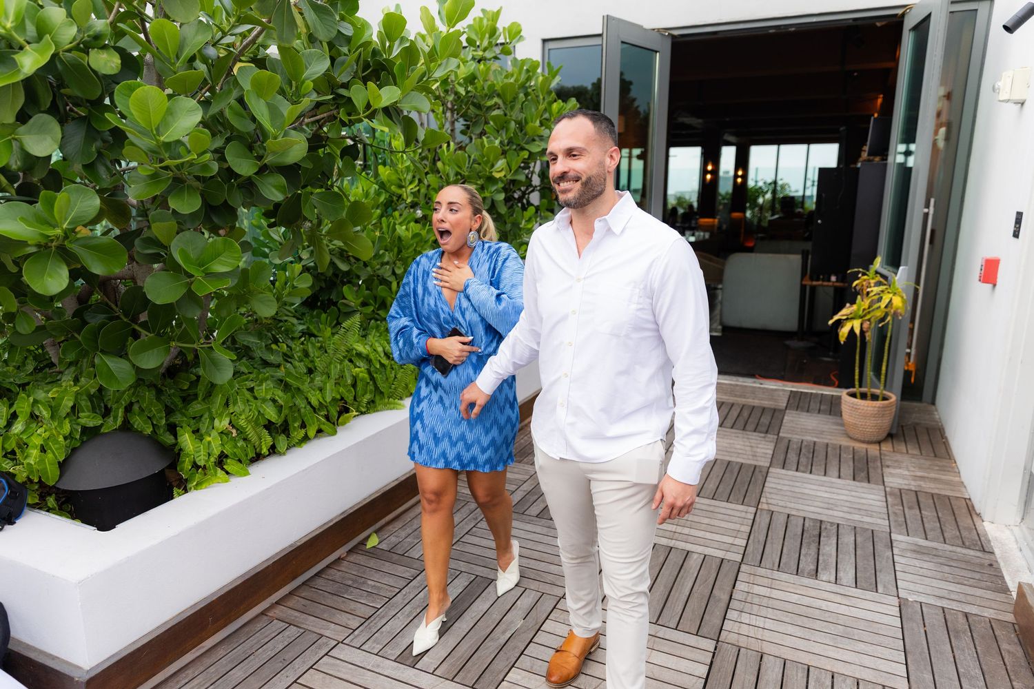 A group of guests walk along a wooden deck pathway with tropical plants and foliage in the background.