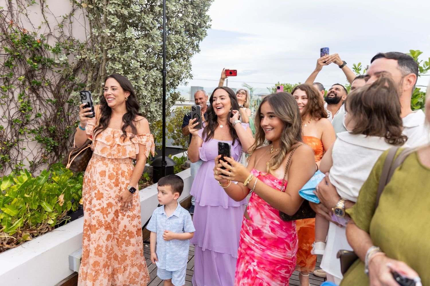 A group of people celebrate outdoors on a sunny day wearing colorful summer attire.