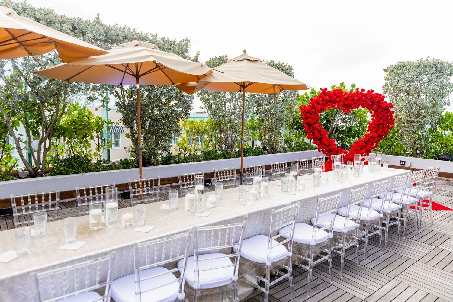 An outdoor patio deck setup for a wedding reception with white chairs, orange umbrellas and a romantic heart decoration.