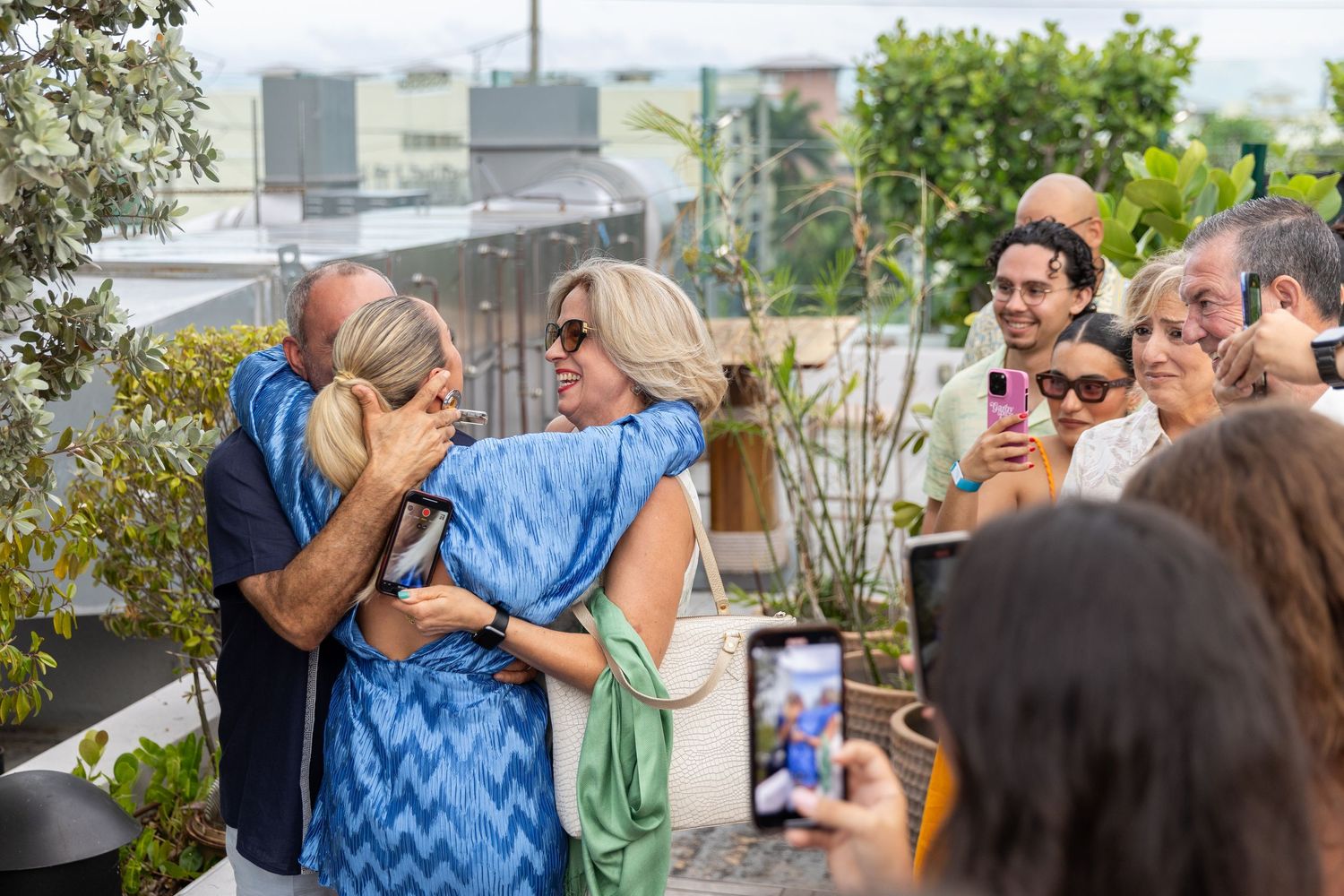 A group gathers for celebration photos on a rooftop terrace with city buildings in the background.