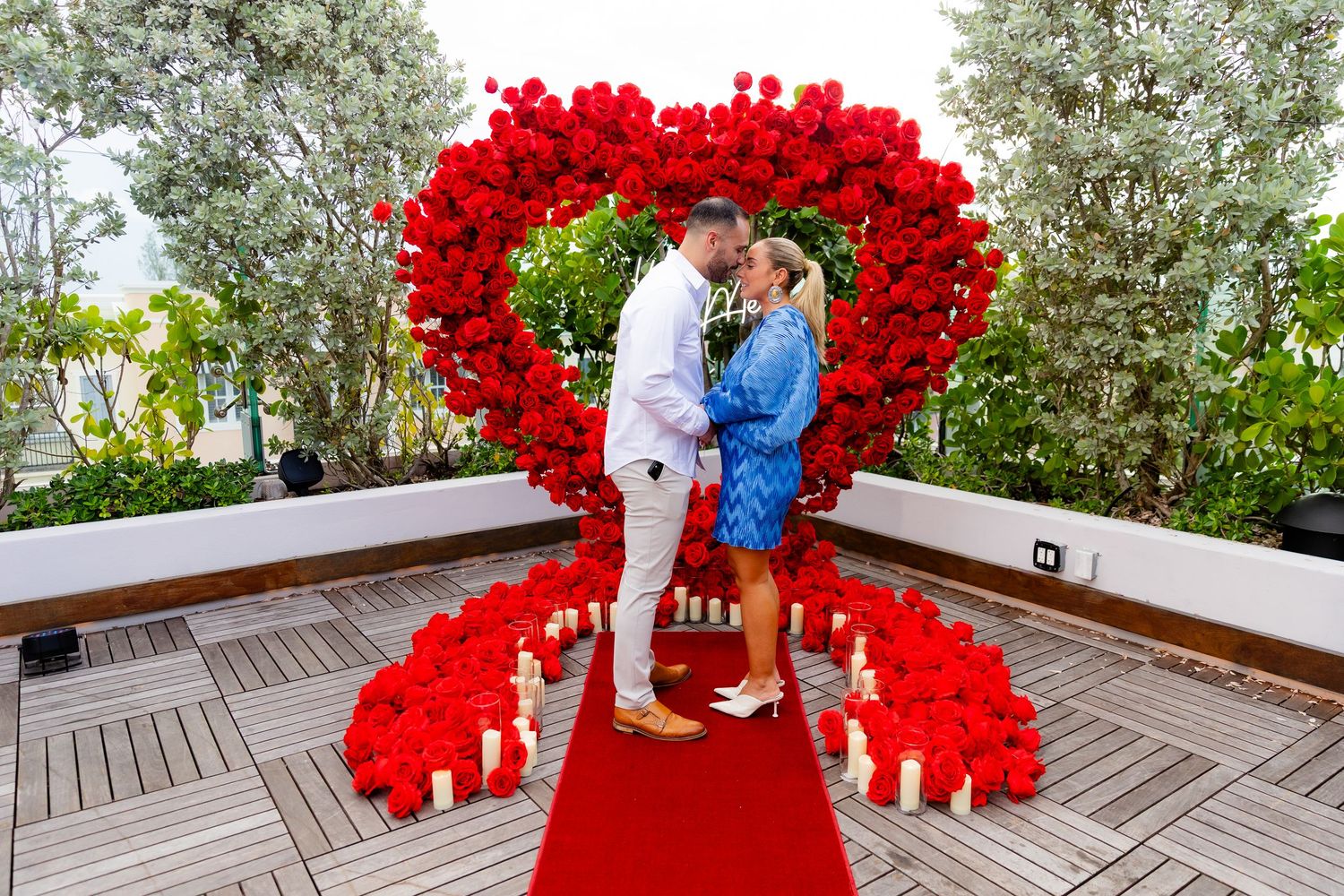 Romantic proposal moment captured under a stunning red heart balloon arch installation.