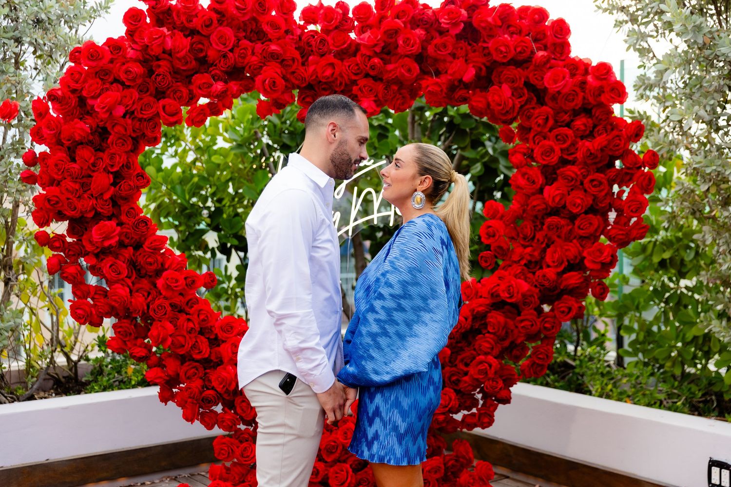 A beautiful outdoor proposal scene with a dramatic red heart-shaped balloon arch on a deck.