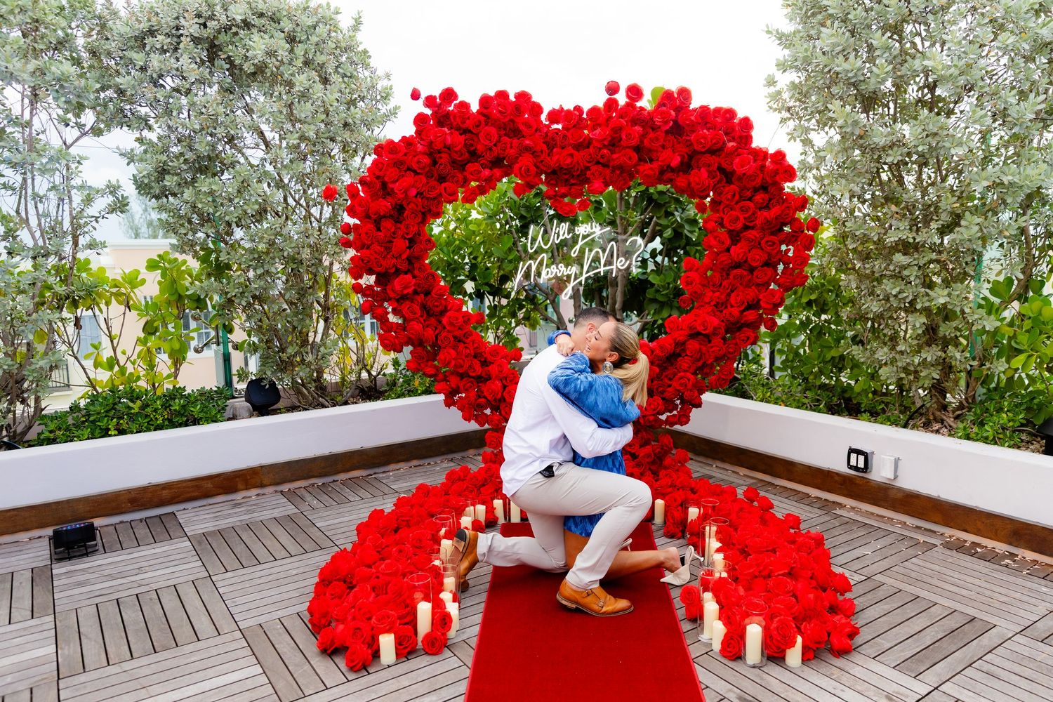 Romantic red rose heart display on wooden deck with trees in background and soft lighting.