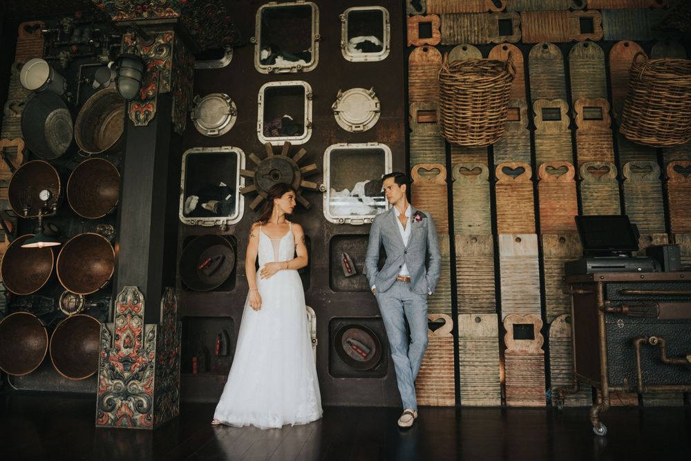 Wedding couple poses against rustic brick wall with vintage decor and frames in moody lighting.