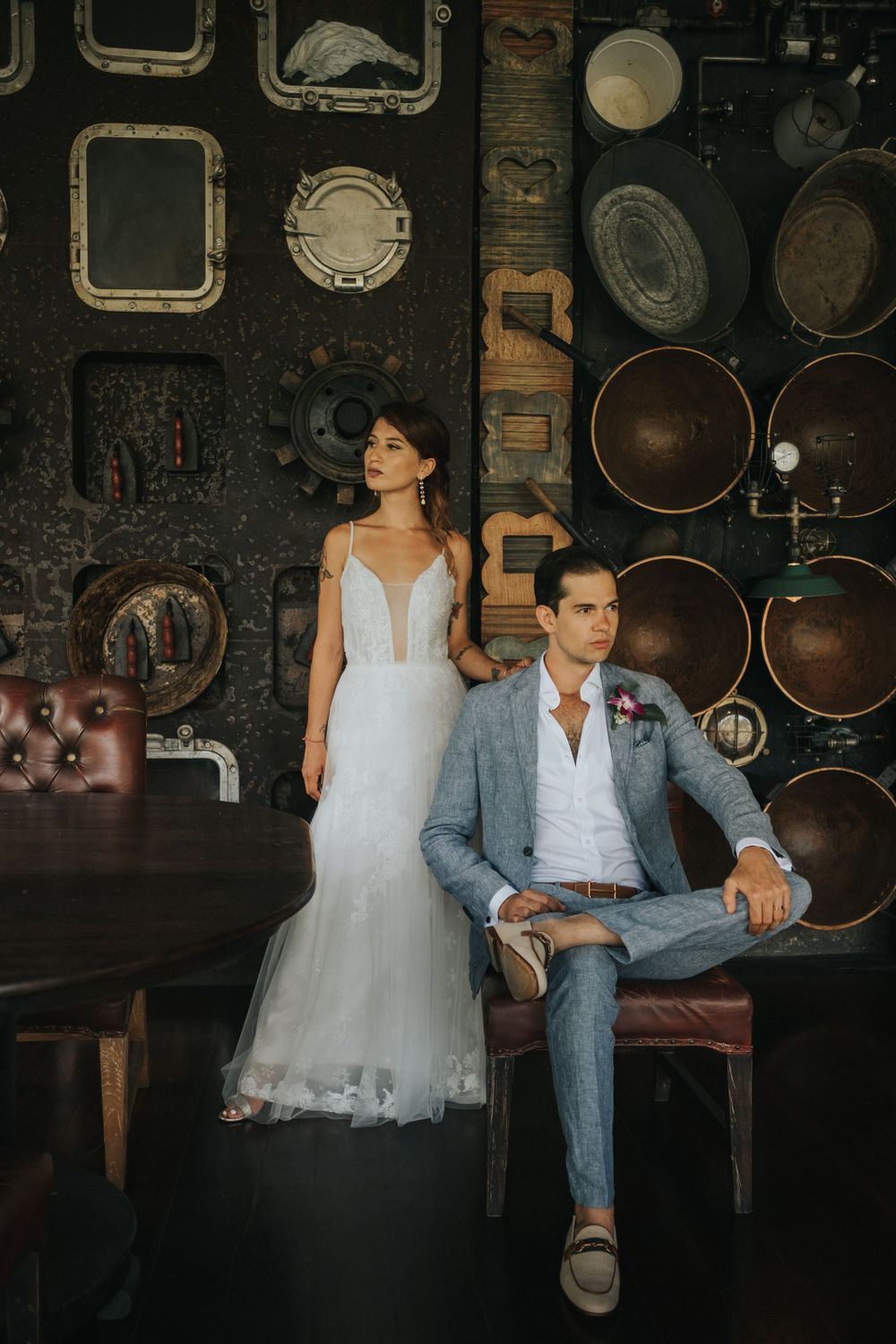 Artistic wedding portrait in dark room with vintage frames and rustic wall decor.
