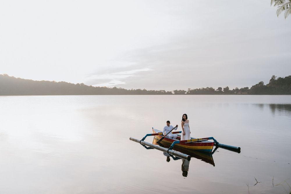 A traditional wooden outrigger boat floats on calm waters at sunset with mountains in the distance.