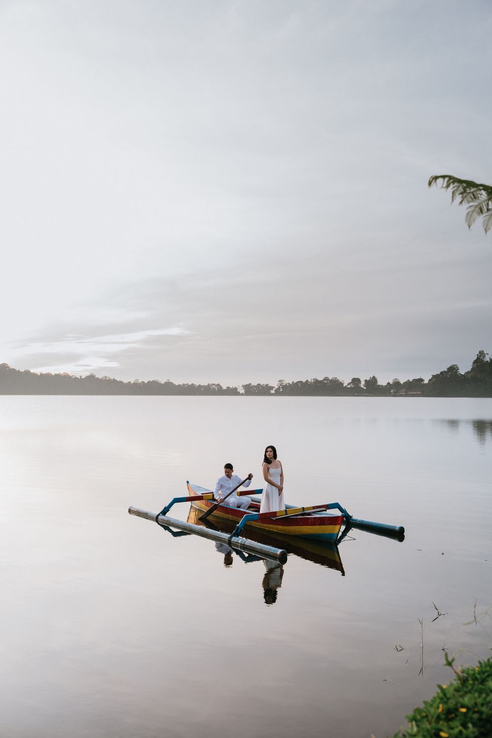 A serene lake scene with an outrigger boat floating on still waters at dusk.