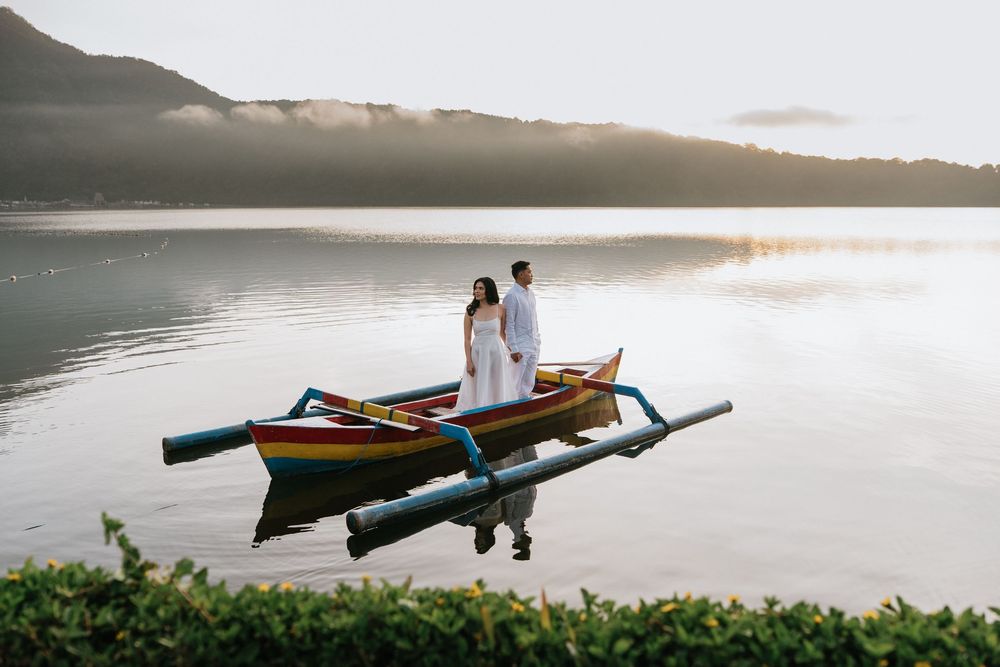 A wooden outrigger boat glides across peaceful waters with mountains silhouetted in the background.