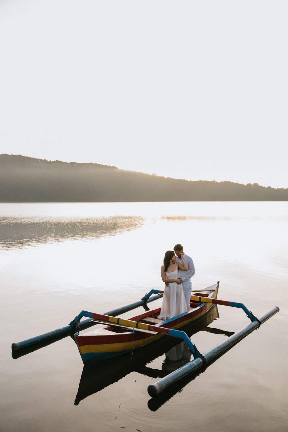 A couple shares an intimate moment in a traditional wooden boat on calm waters at sunset.