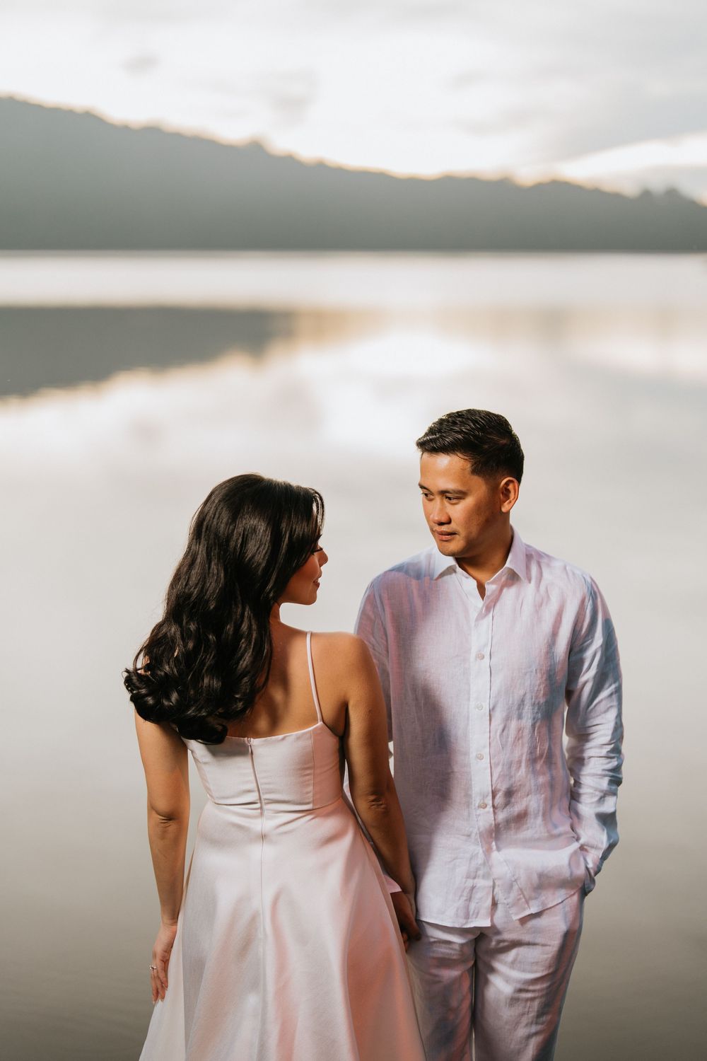 Couple in white outfits sharing intimate moment by serene lake.