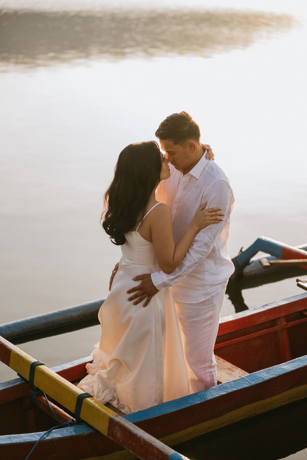 Romantic couple embracing in traditional wooden boats on calm waters during sunset.
