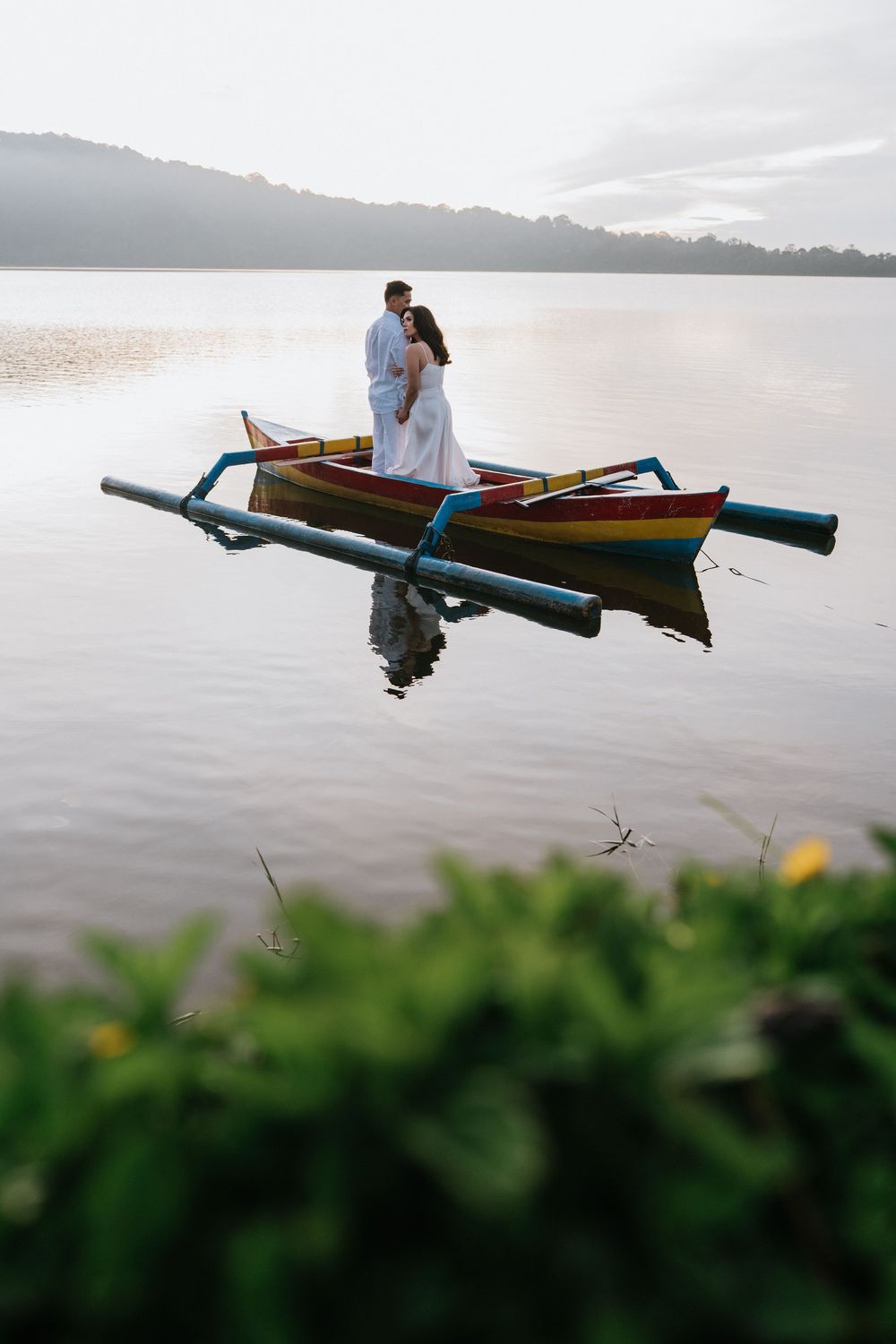 A couple sits in a traditional wooden outrigger boat on tranquil waters during golden hour.
