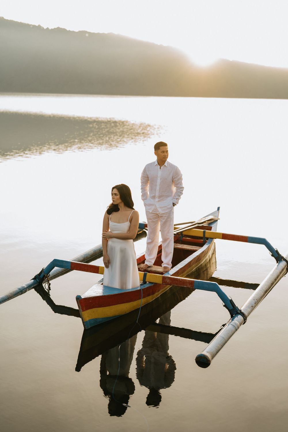 Couple sitting in traditional wooden boat on calm lake during sunset.