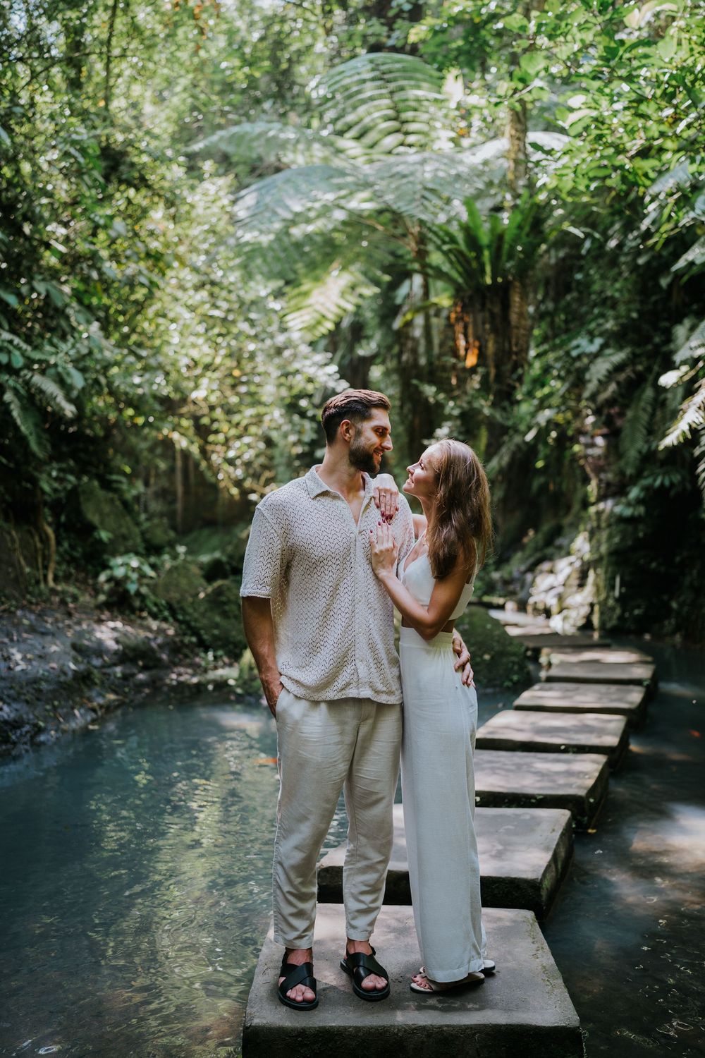 Romantic couple standing together on wooden walkway over turquoise water in tropical setting.