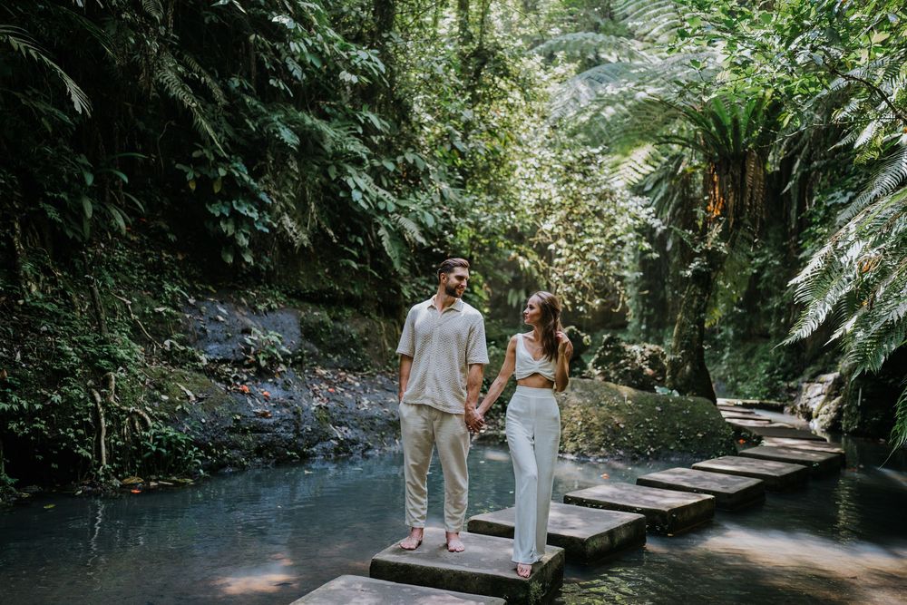 Couple sharing intimate moment on wooden bridge over tranquil blue water surrounded by jungle.