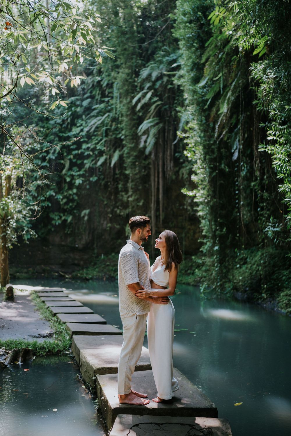 Romantic moment captured on wooden bridge surrounded by tropical greenery and blue water.