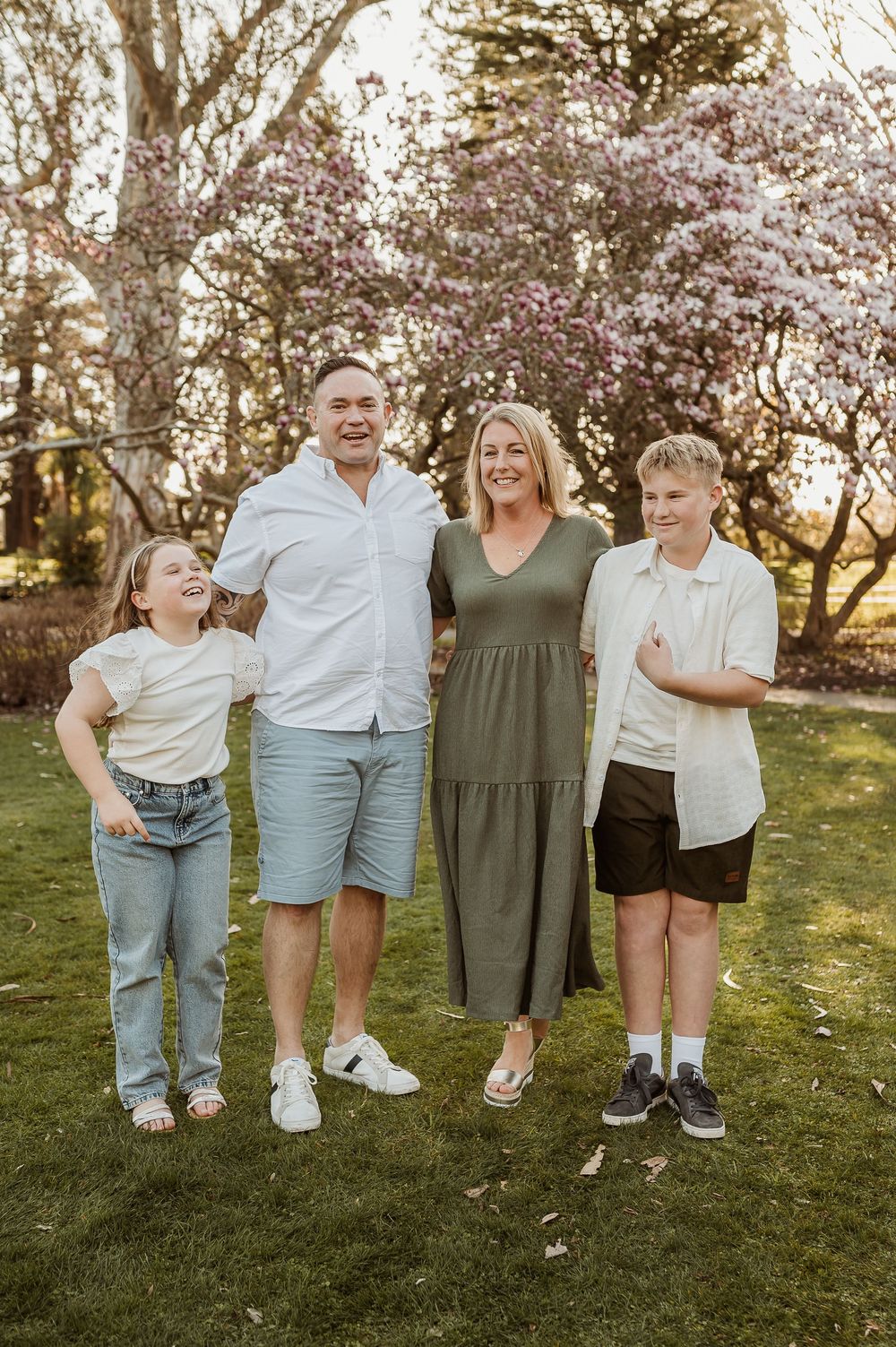 Artistic cropped photo showing legs and feet of people standing in a row on grass with spring blossoms in background.