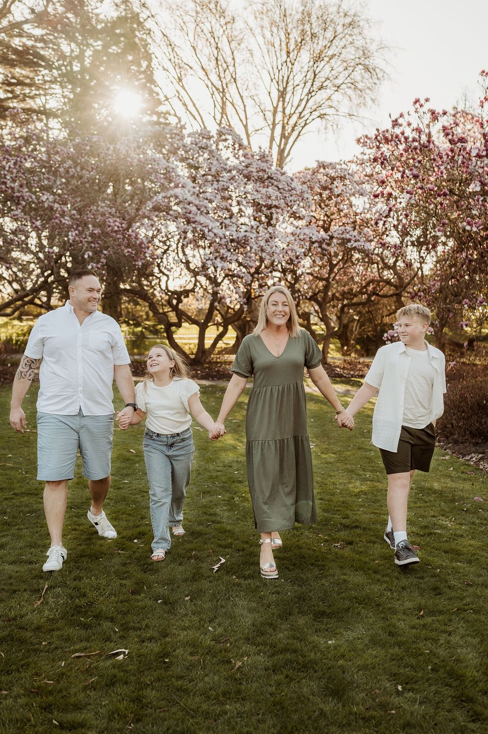 Family enjoys a springtime photo session in a blooming orchard at sunset with cherry blossoms in the background.