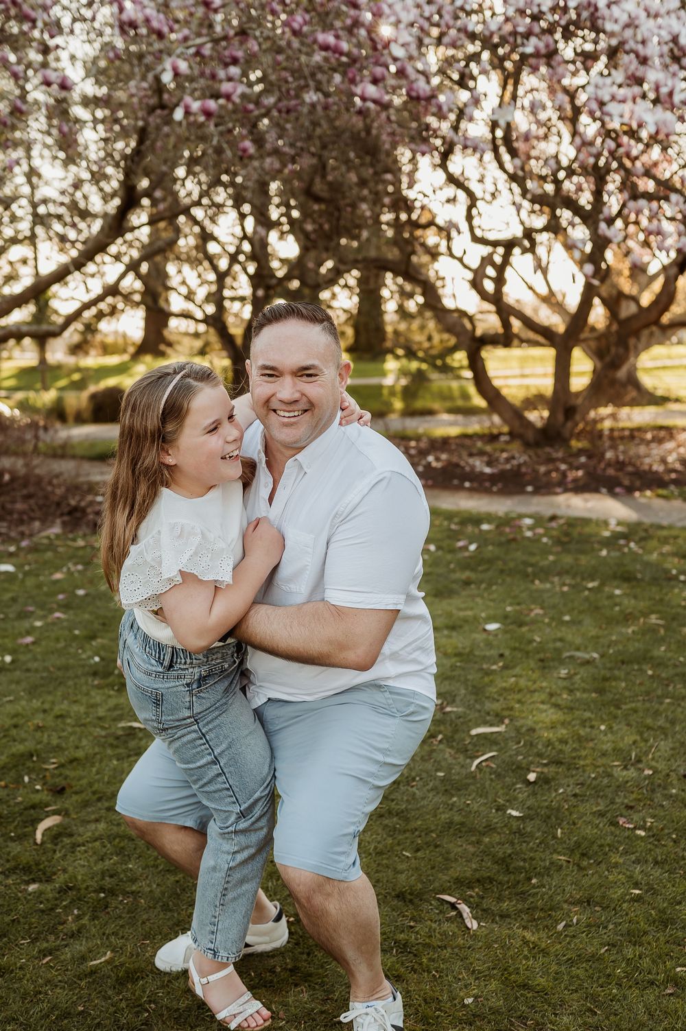 Candid outdoor portrait of parent and child laughing together in a blooming garden at sunset.