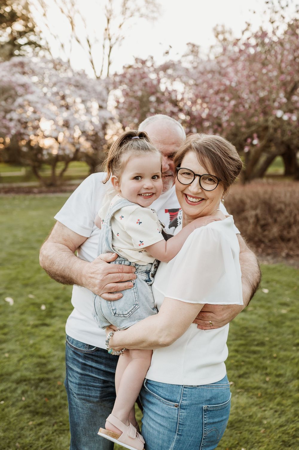 A family smiles together while standing in a blooming spring garden with cherry blossom trees in the background.