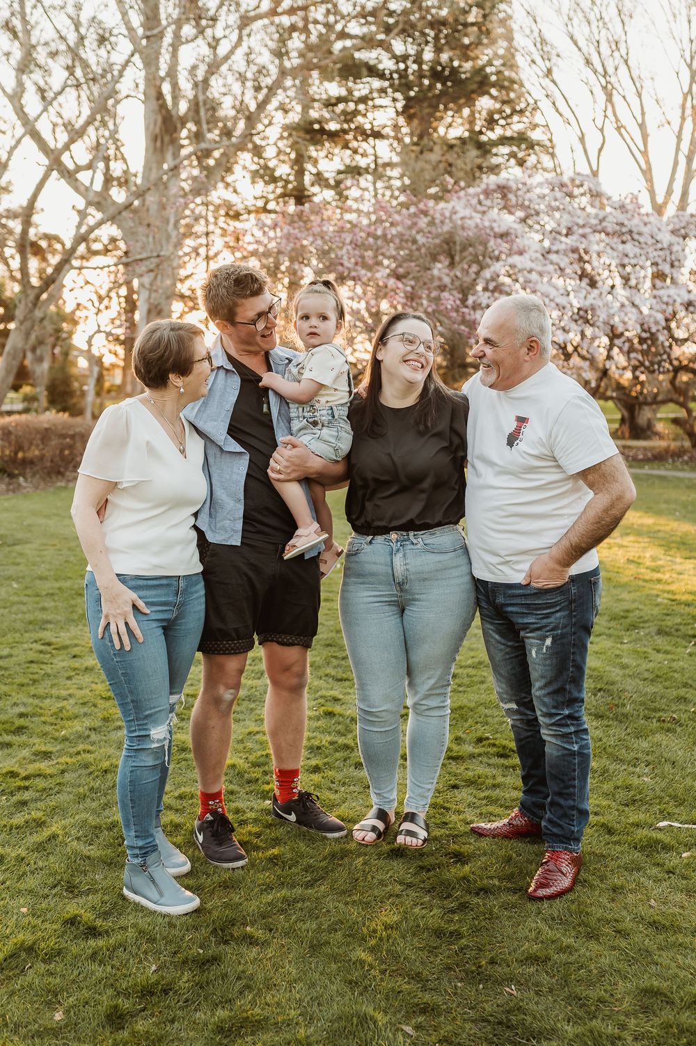 Family shares joyful moments together during outdoor photo session at sunset in grassy field.