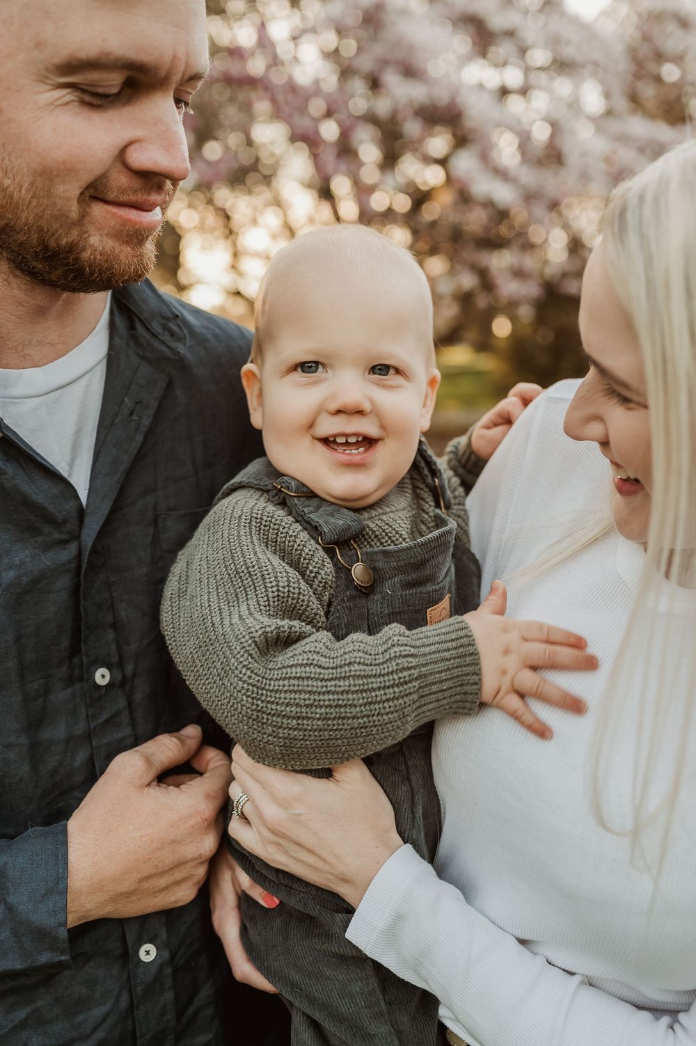 A tender family moment captured outdoors with smiles and laughter against a backdrop of cherry blossoms.