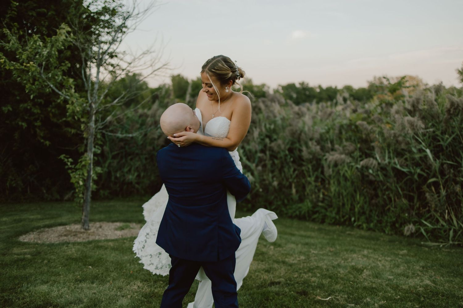A couple embraces during an outdoor evening photo session in a garden setting with lush greenery.