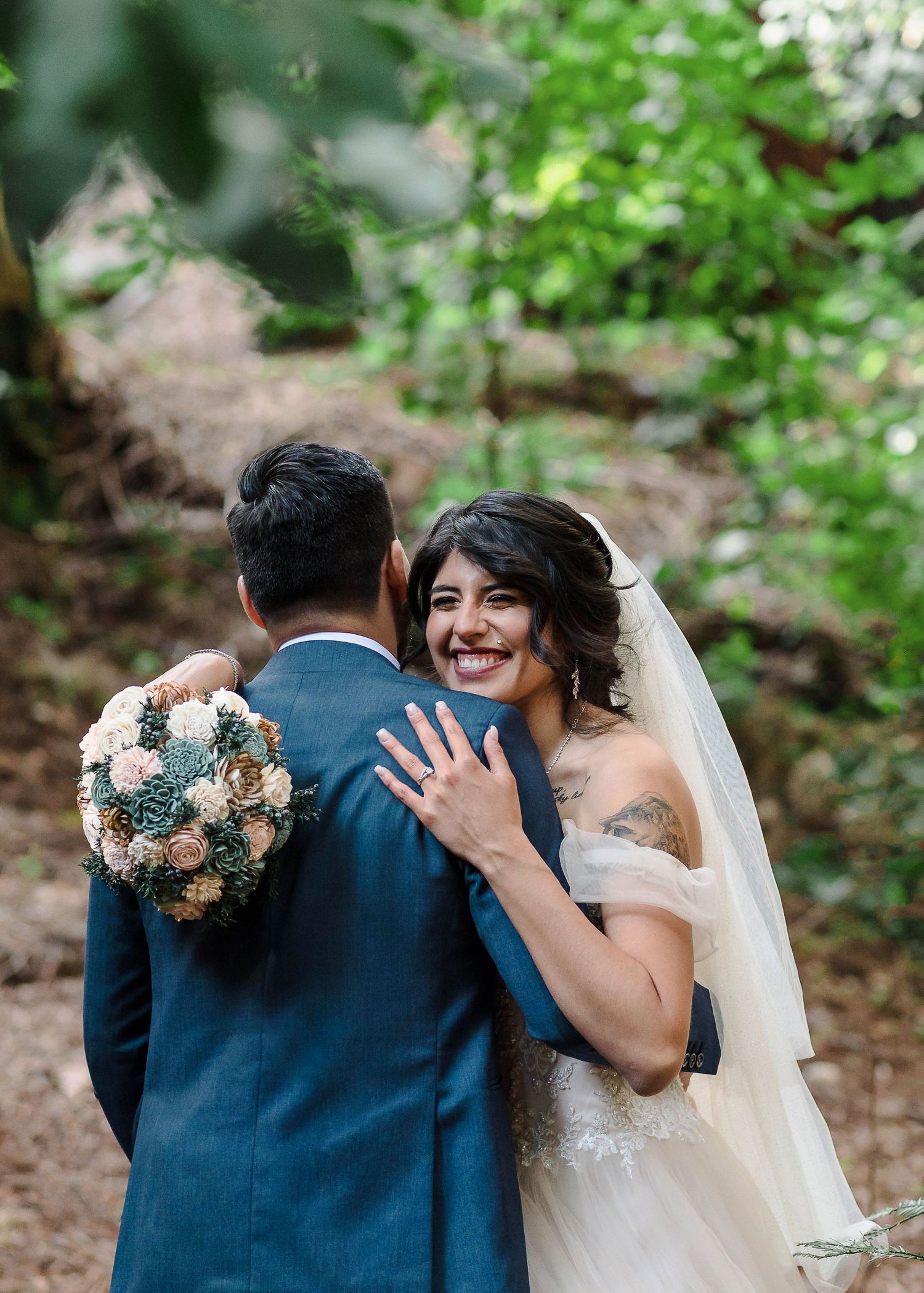 A lush floral arrangement with white roses and greenery hangs suspended from a wooden beam in a forest setting.