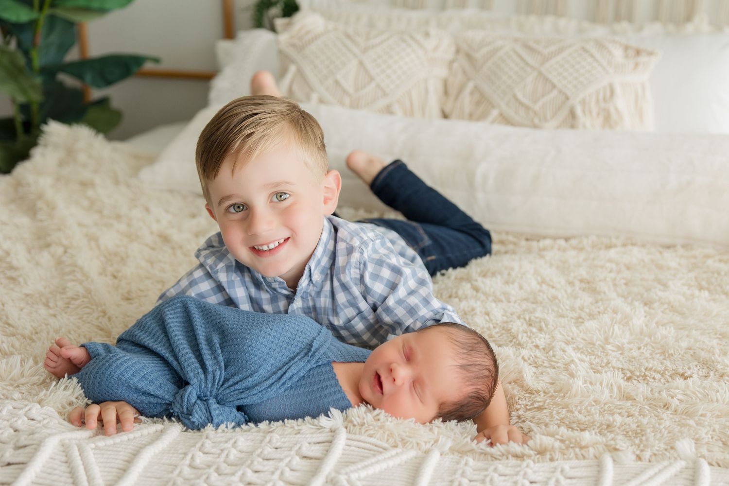Two children lying together on cream colored bedding with one in a plaid shirt and one in blue clothing.