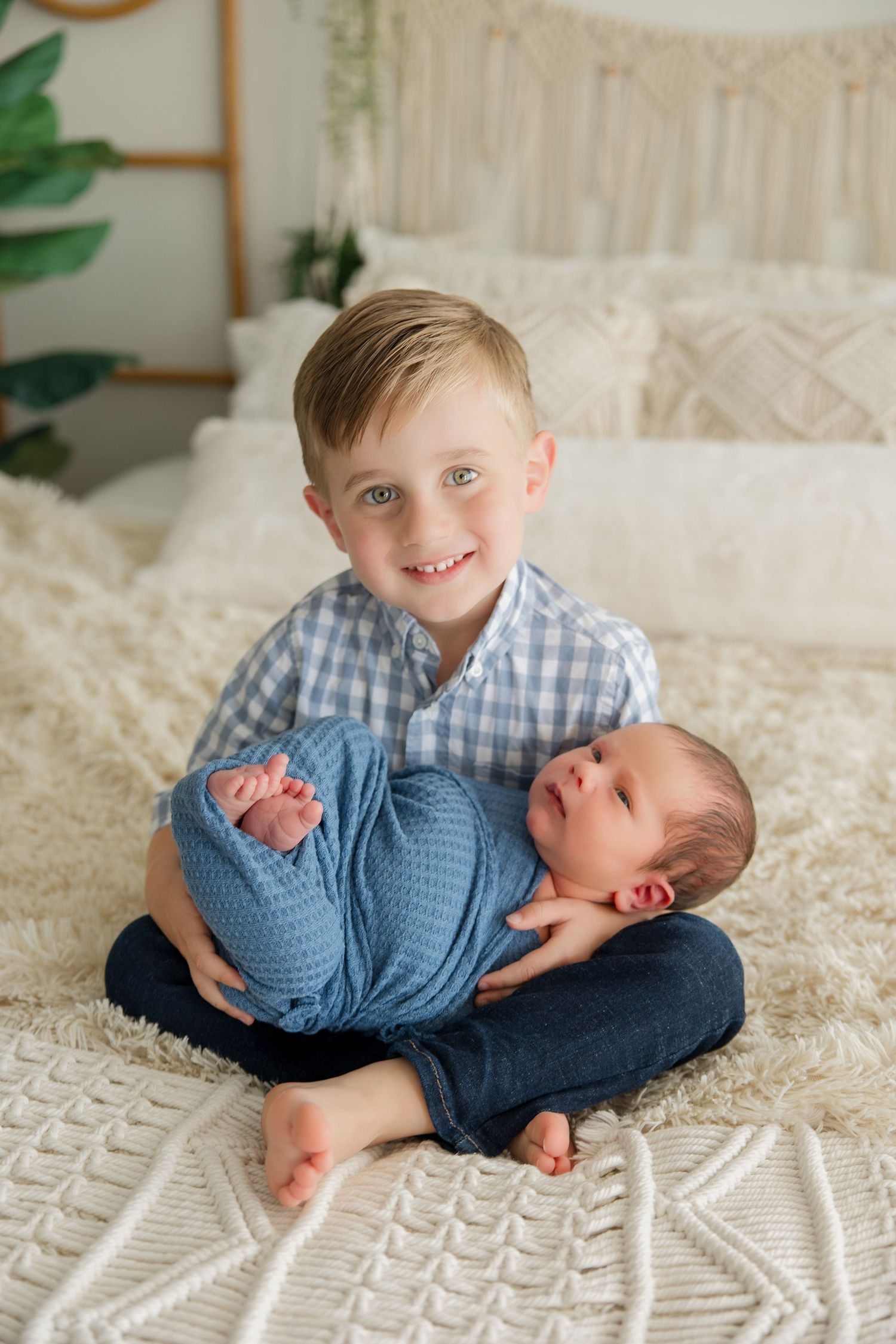 Sweet sibling poses with their newborn on a textured white blanket showing tender affection.