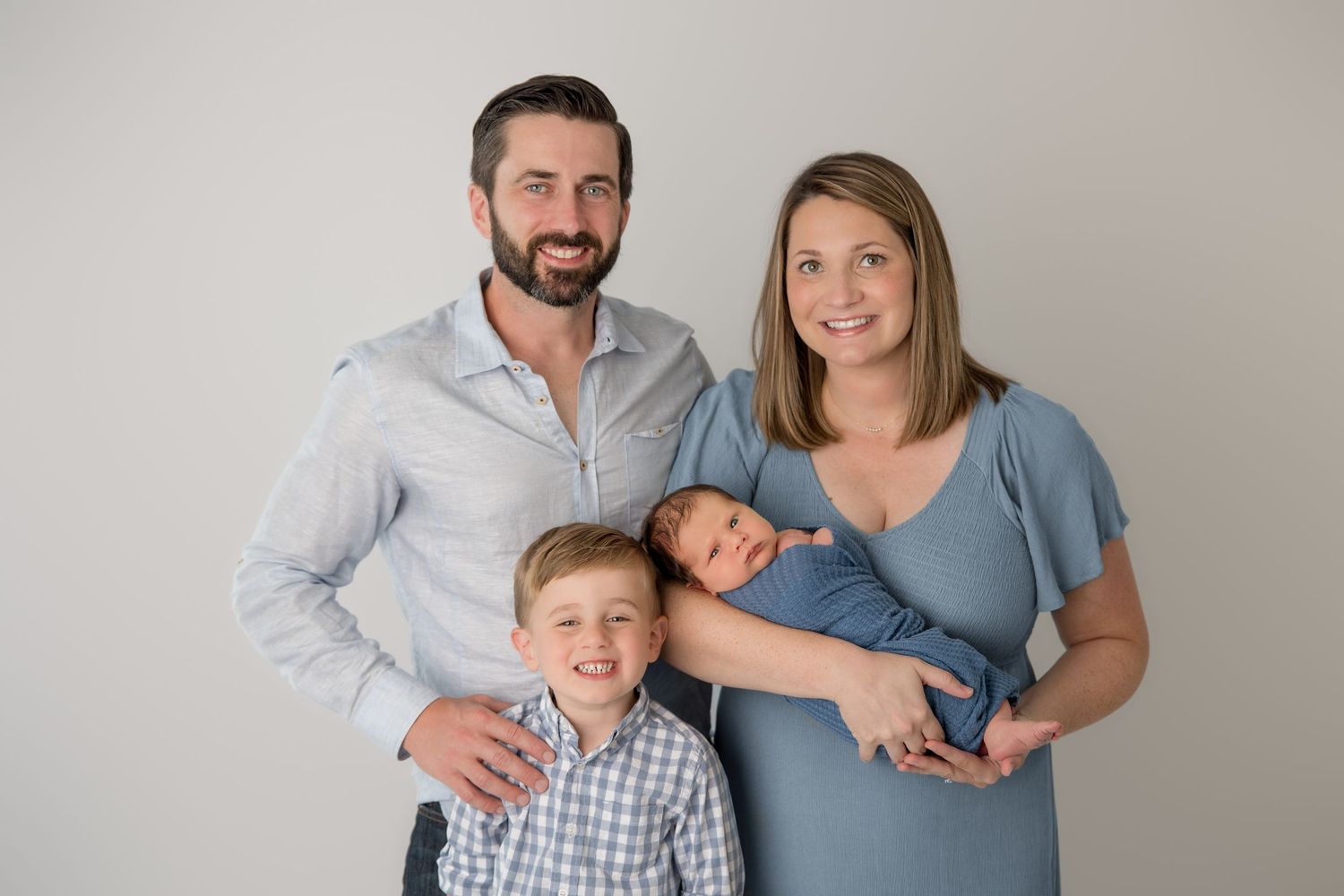 A family wearing coordinated grey and white outfits poses together for a studio portrait against a neutral background.