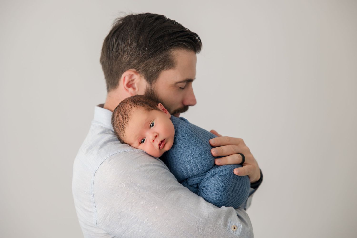 Close up portrait of parents cuddling with their newborn in simple white and blue tones.
