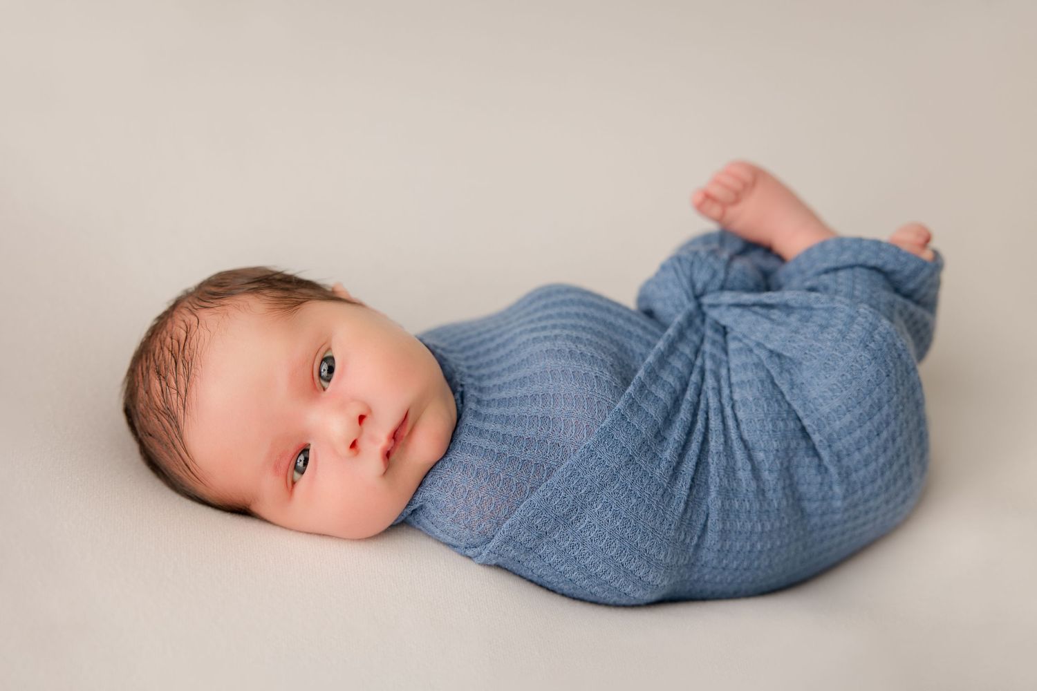 A sleeping newborn in blue onesie photographed from different angles on neutral backdrop.