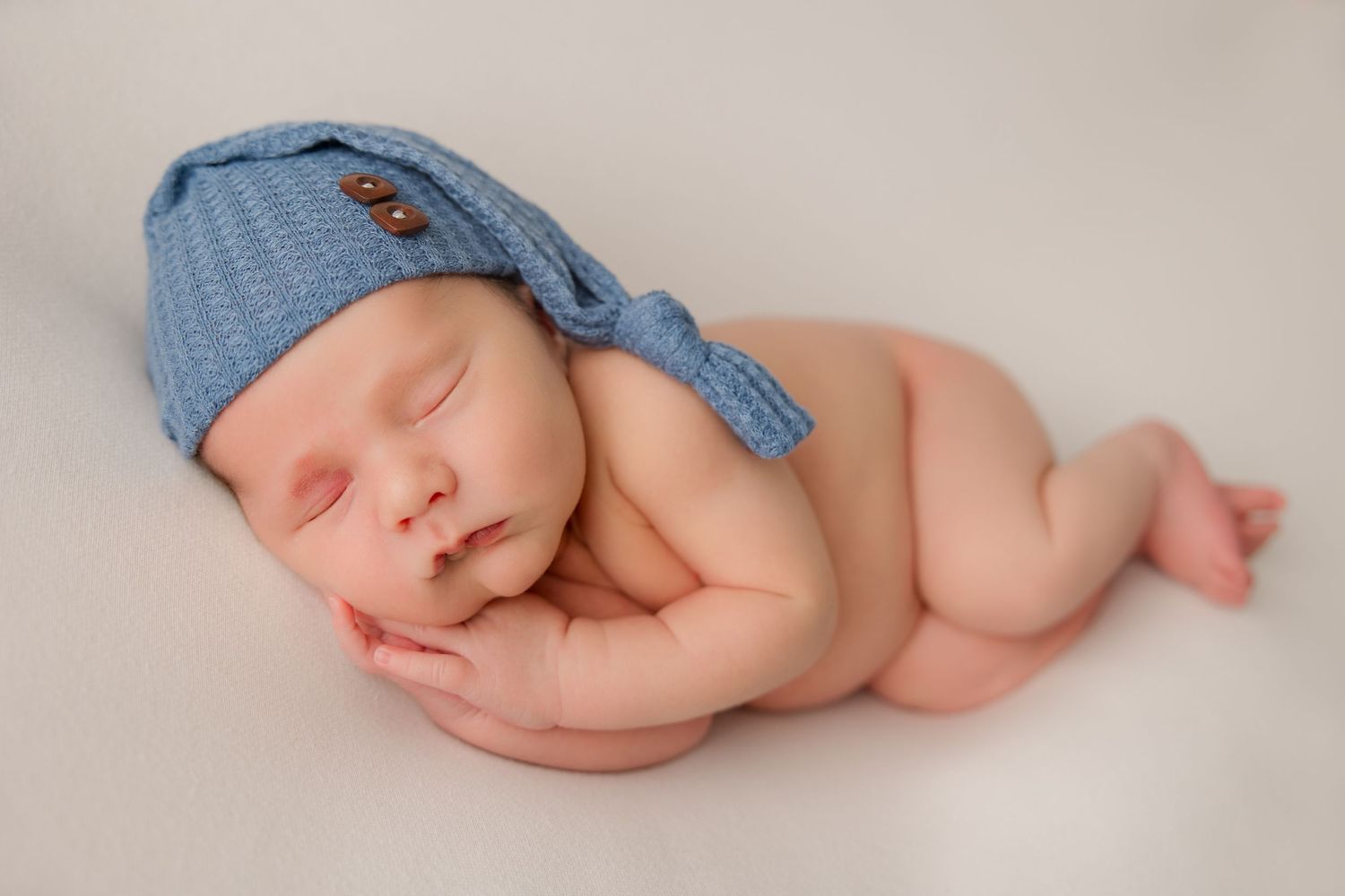 Sleeping newborn baby wearing blue knit hat on white background.