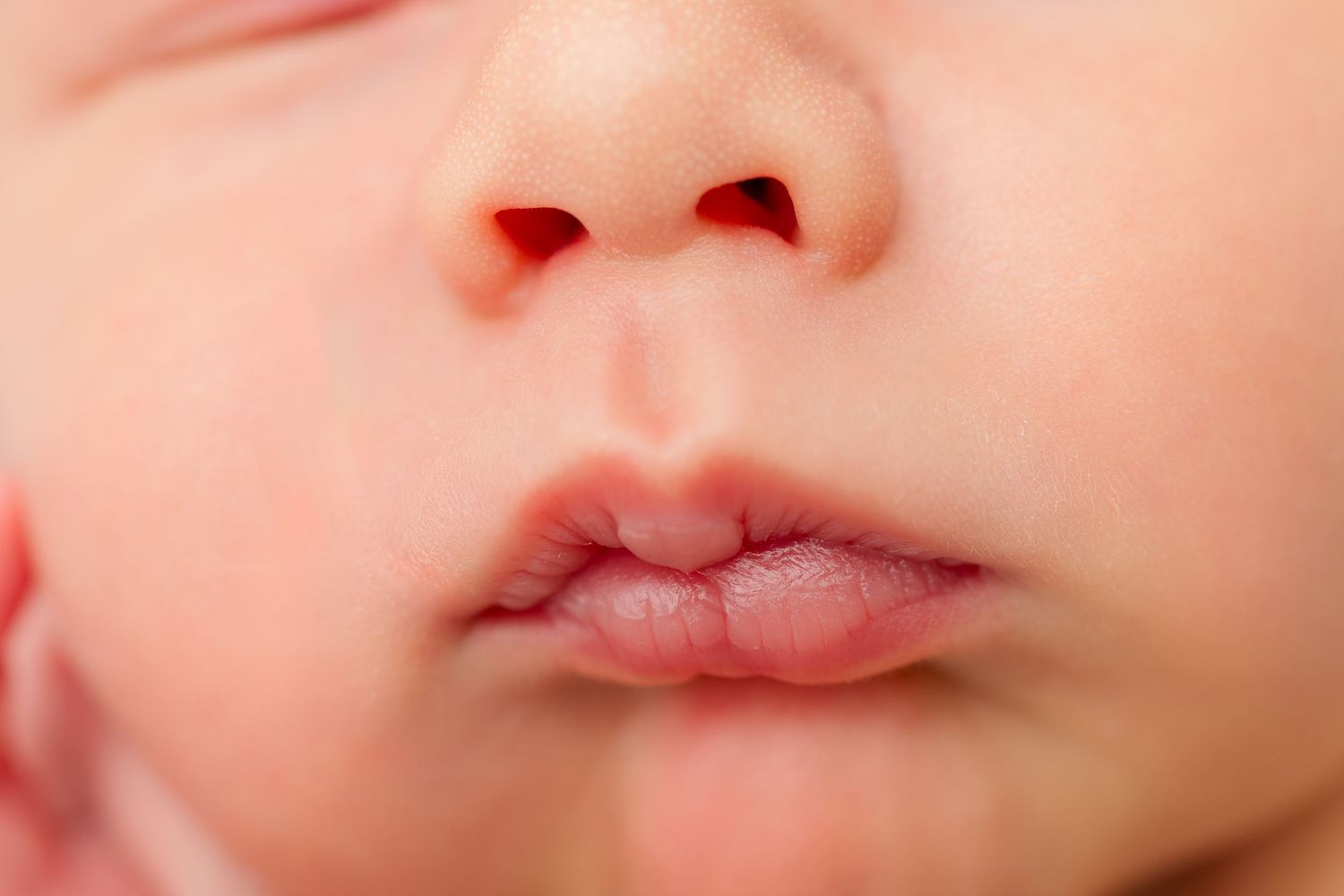 Extreme close up macro shot of a baby's nose and mouth against pink skin tones.