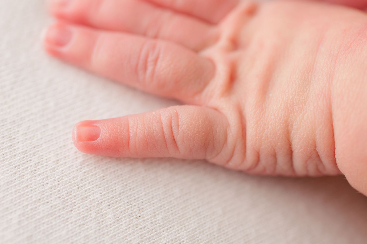 Close-up detail shot of delicate baby fingers on textured fabric.